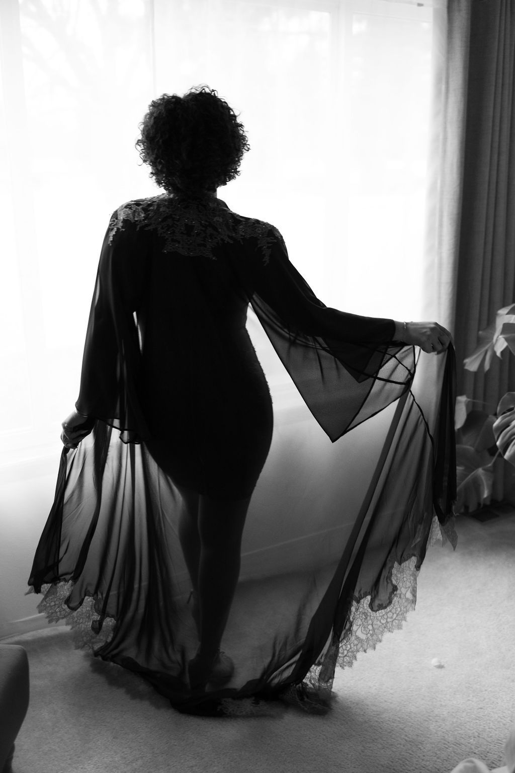 A woman in a long black robe is standing in front of a window.