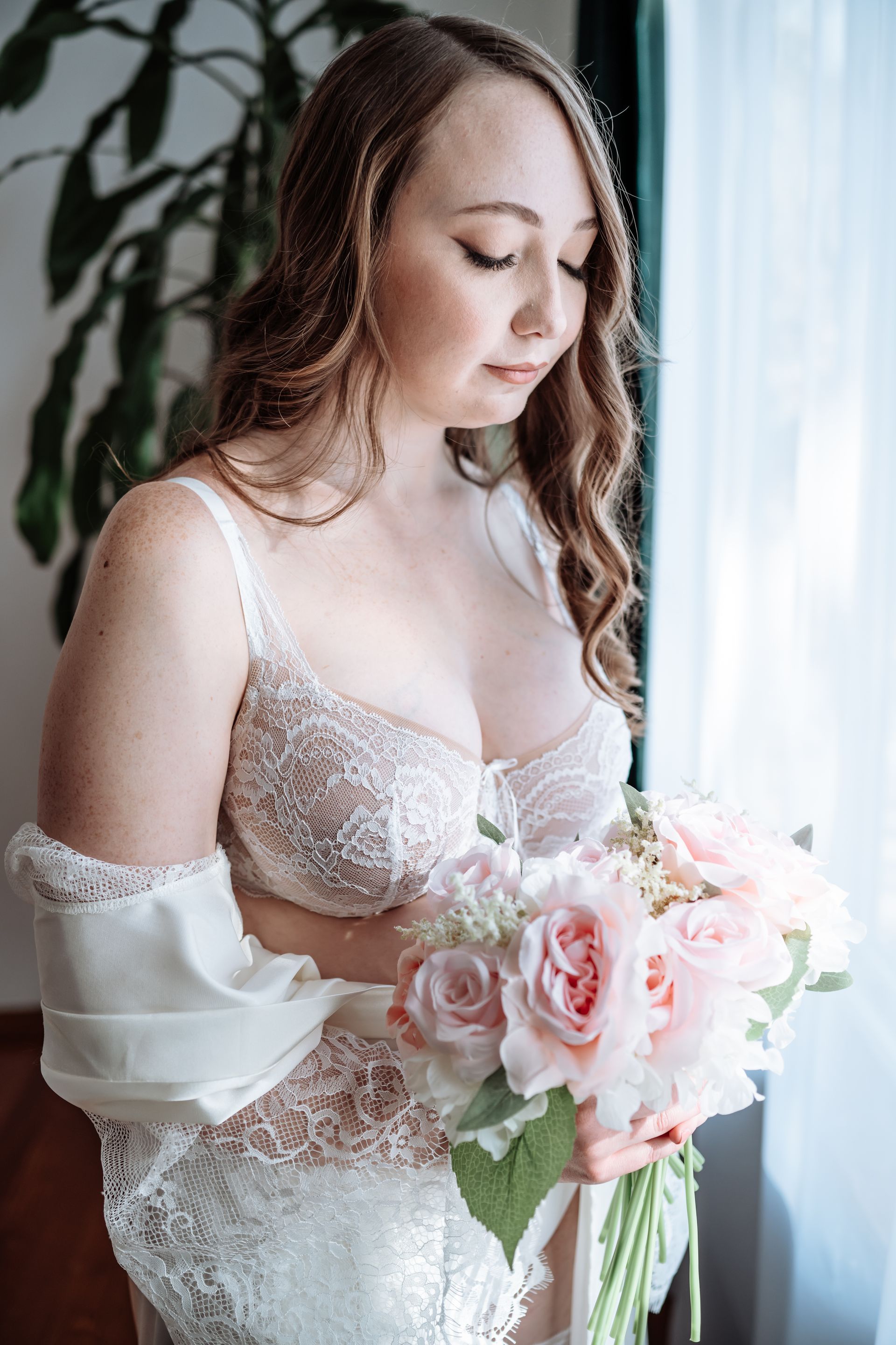 A woman in a white bra is holding a bouquet of pink flowers.
