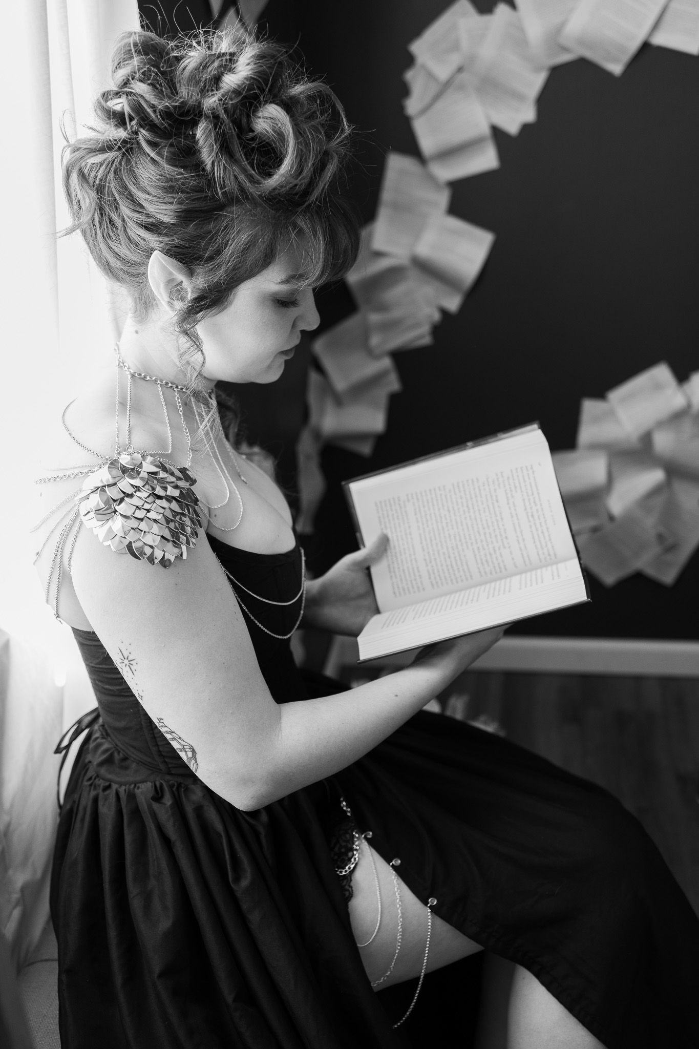 A woman in a black dress is reading a book in a black and white photo.