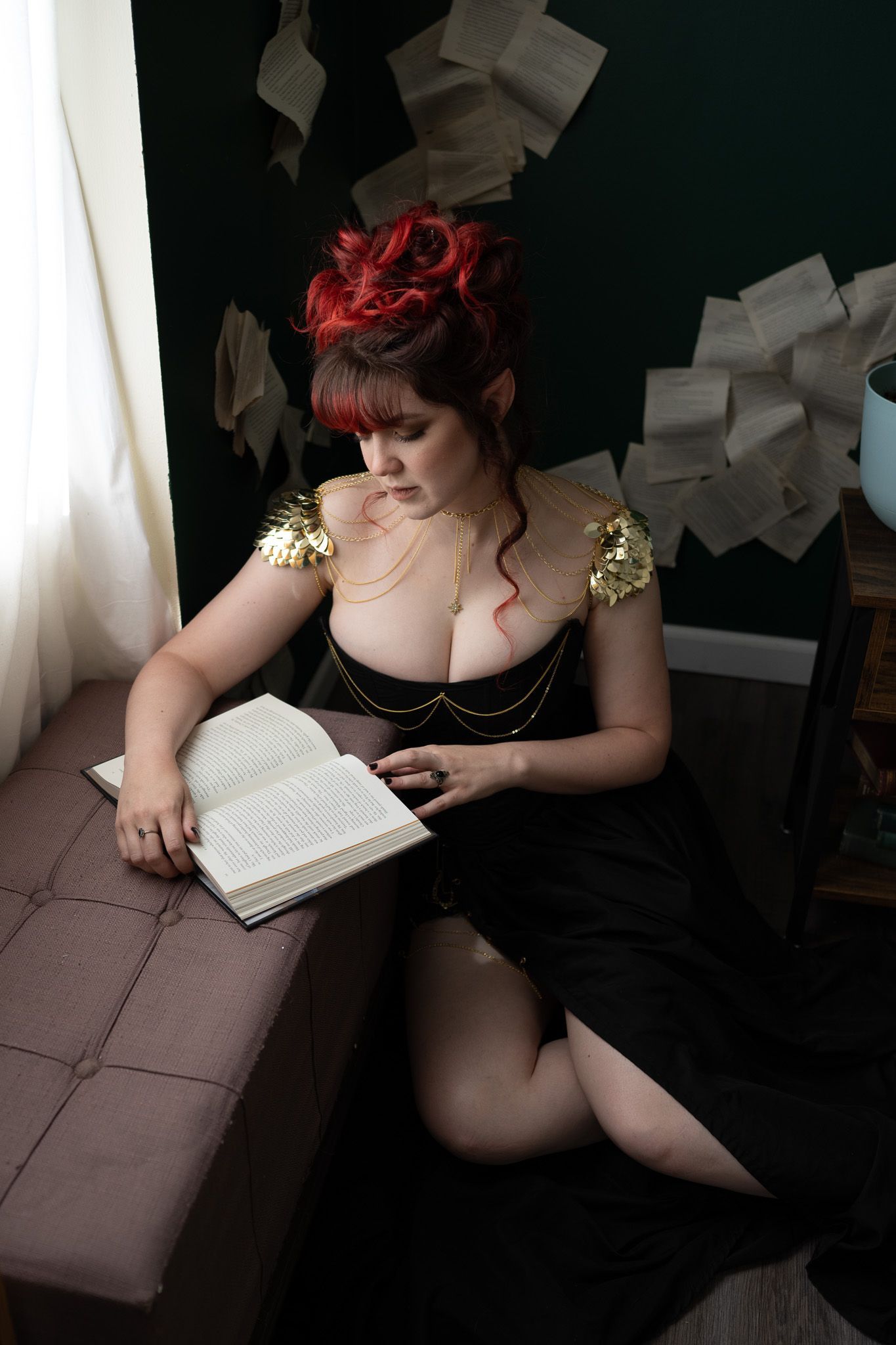 A woman in a black dress is sitting on a bench reading a book.