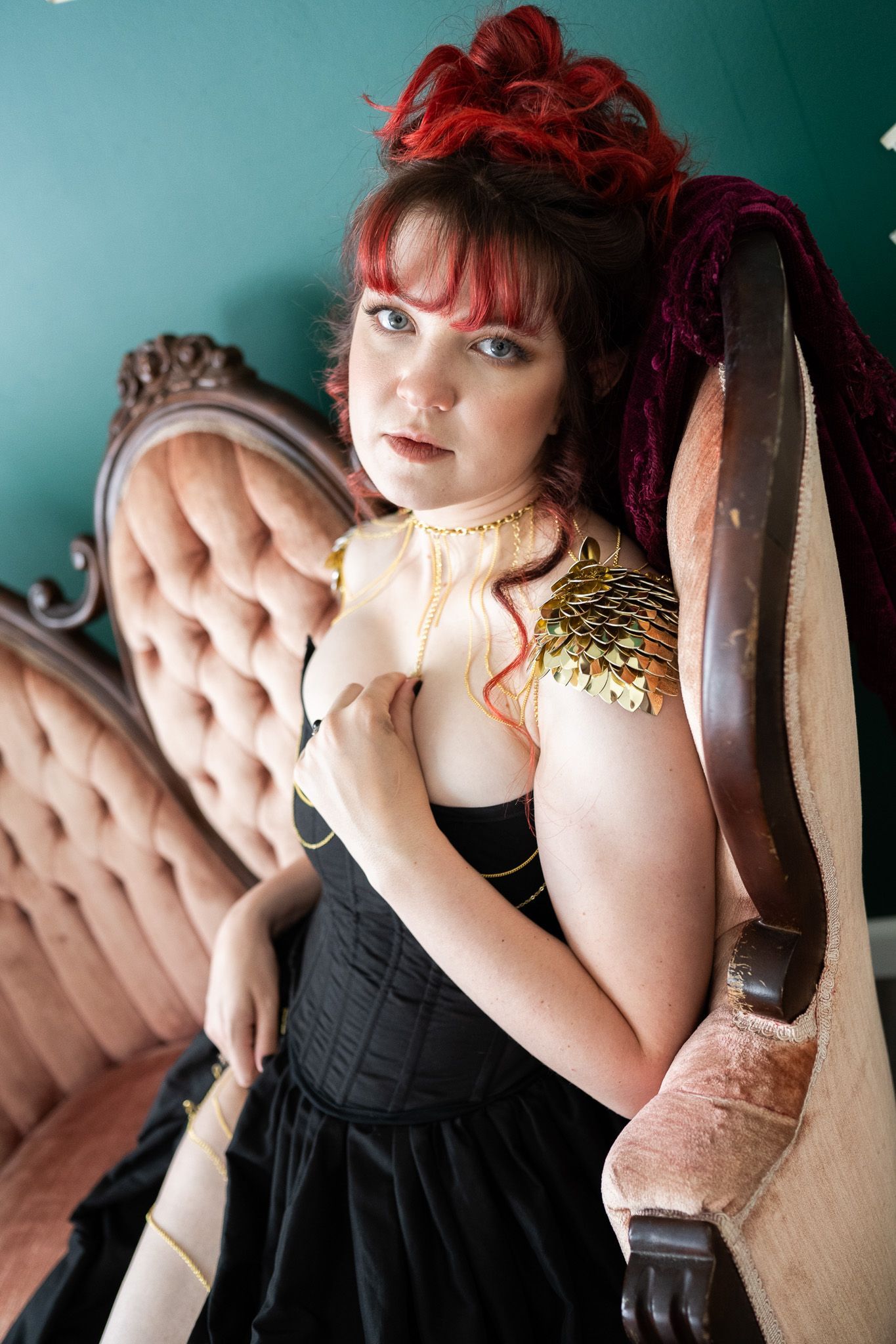 A woman in a black dress is sitting on a couch. She looks like the cover of a romance novel for her boudoir photos.