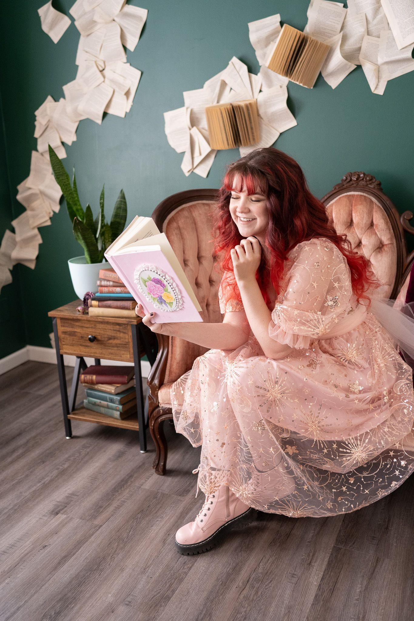 A woman in a pink dress is sitting in a chair reading a book.