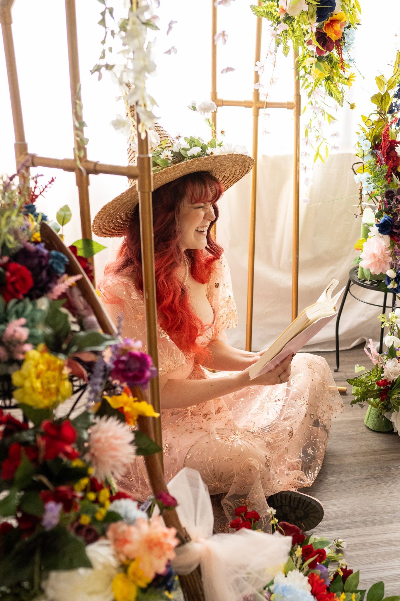 A woman is sitting on the floor reading a book surrounded by flowers.