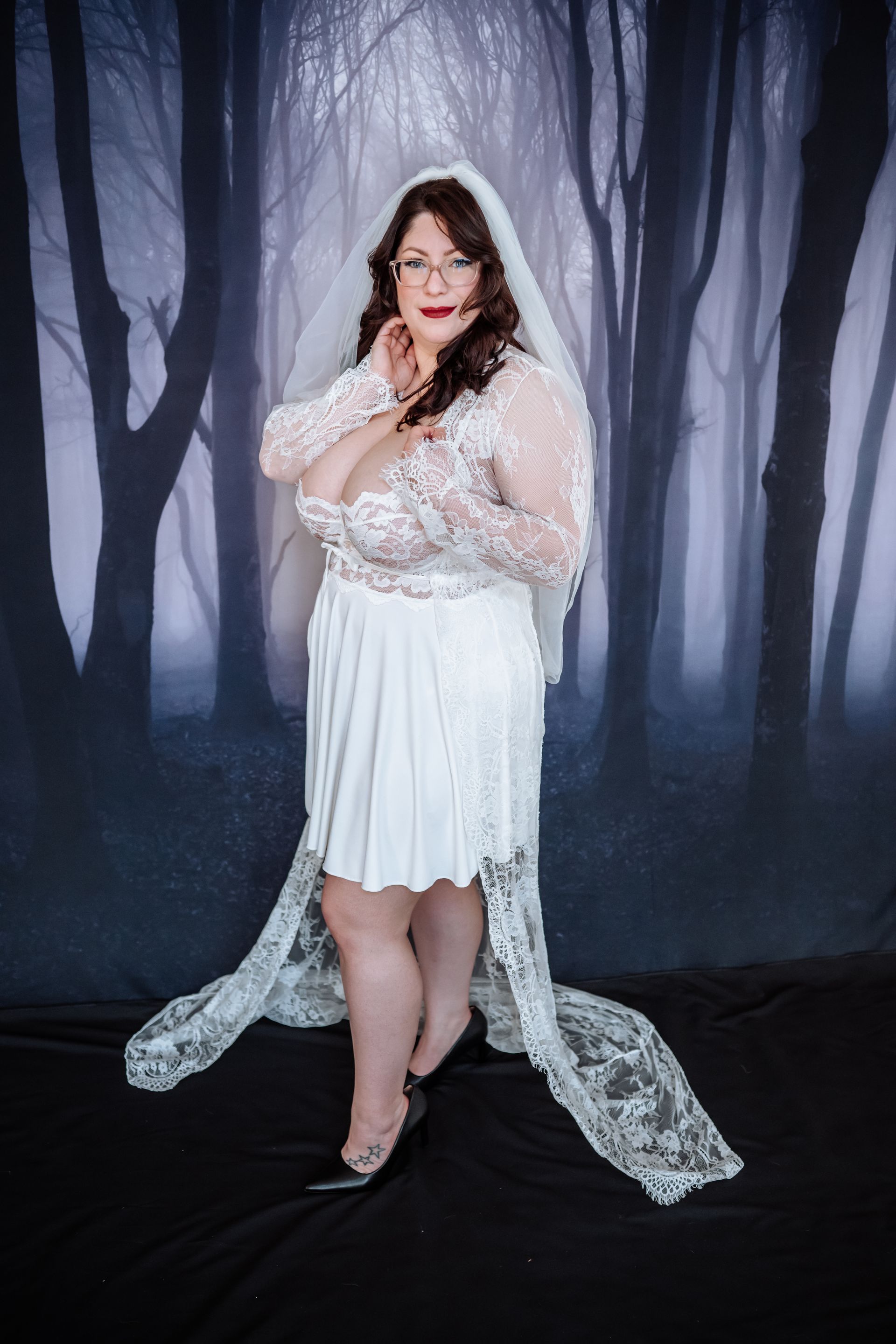 A woman in a white dress and veil is standing in front of a forest.