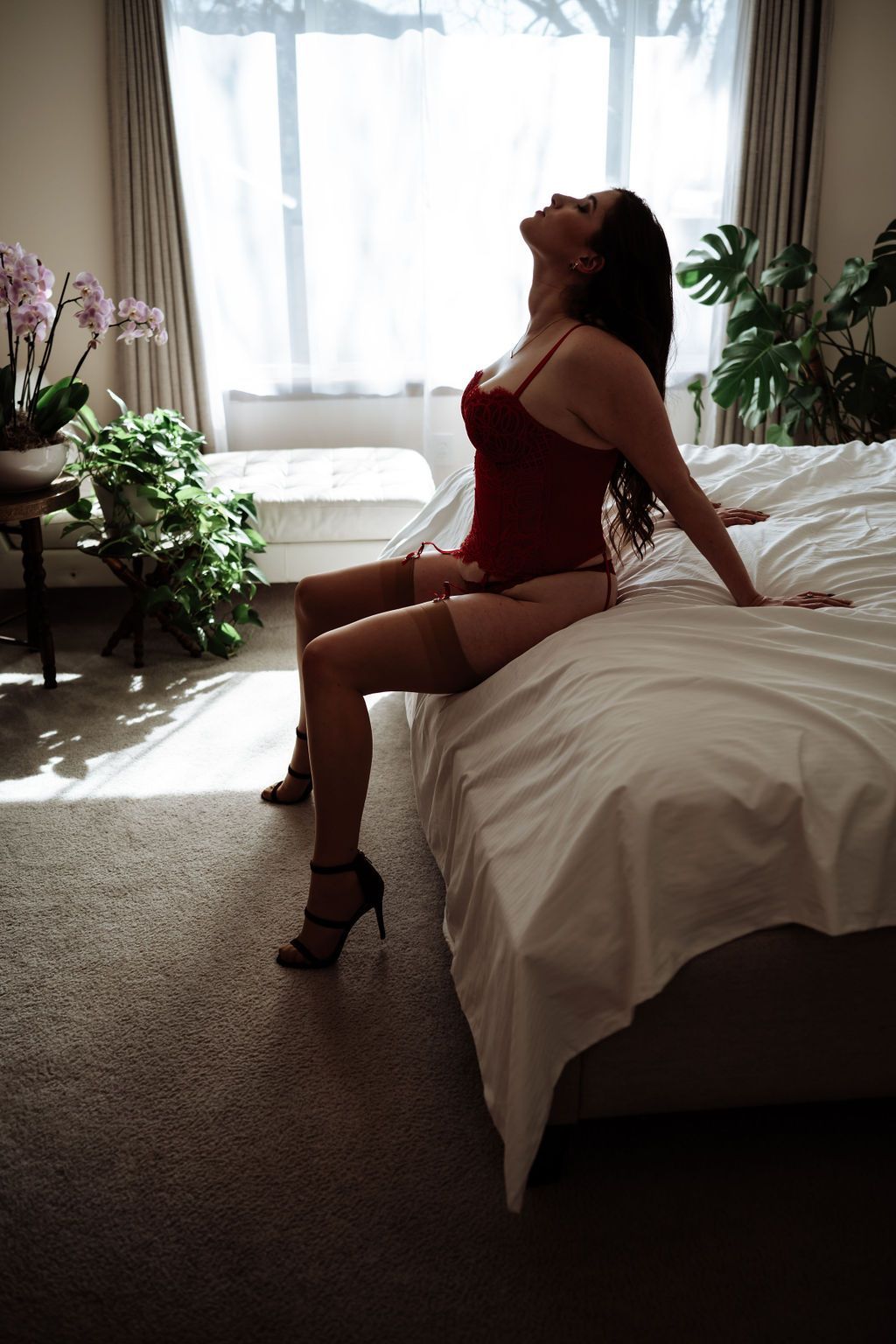 A woman in lingerie is sitting on a bed in a bedroom.