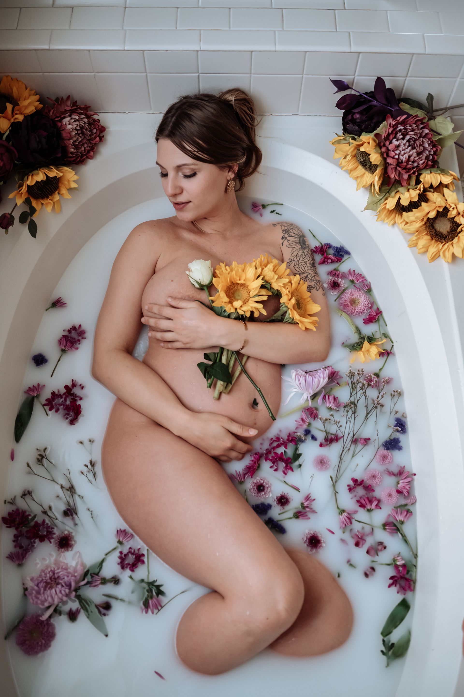 A pregnant woman is laying in a bathtub filled with milk and flowers.