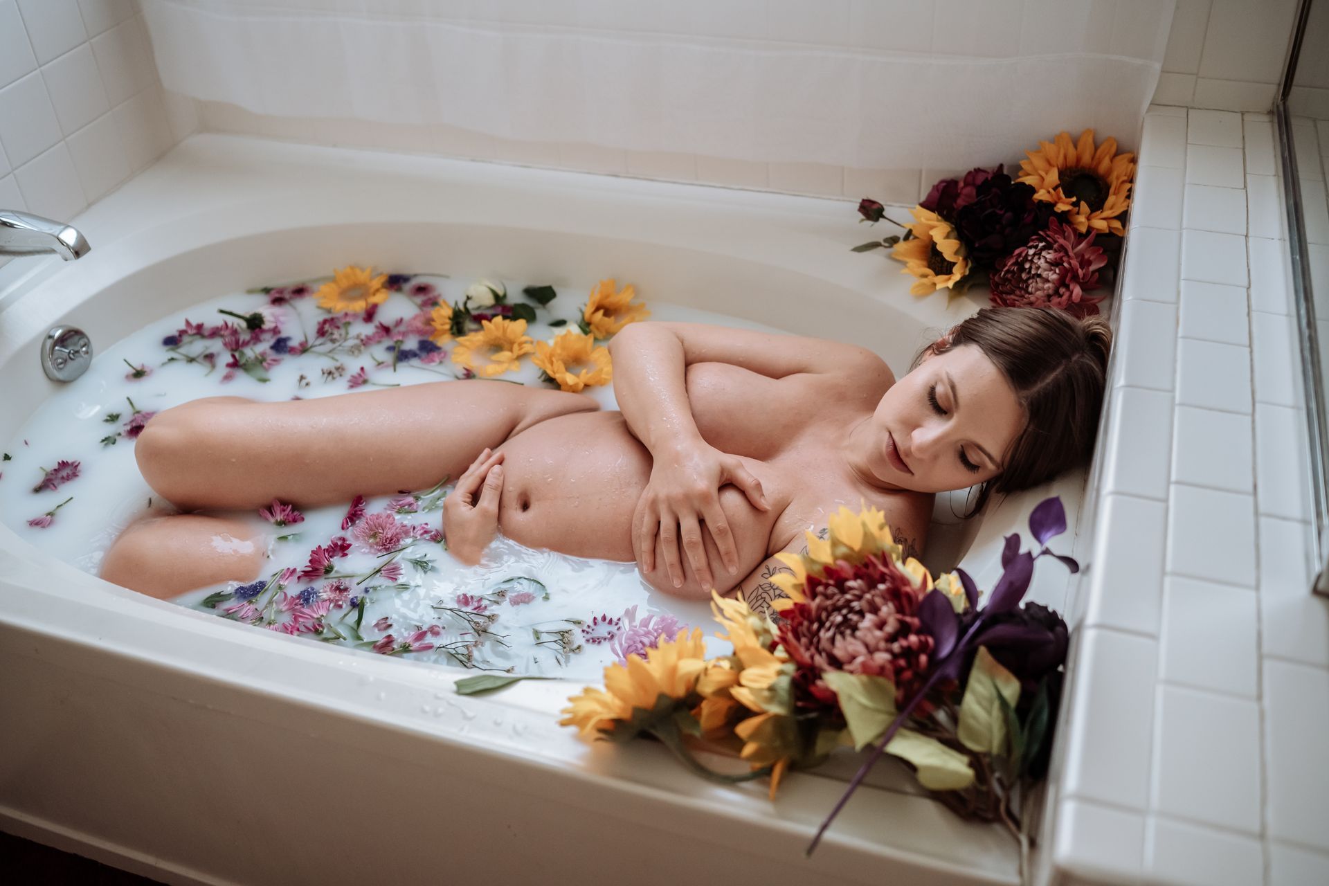 A pregnant woman is laying in a bathtub filled with milk and flowers.