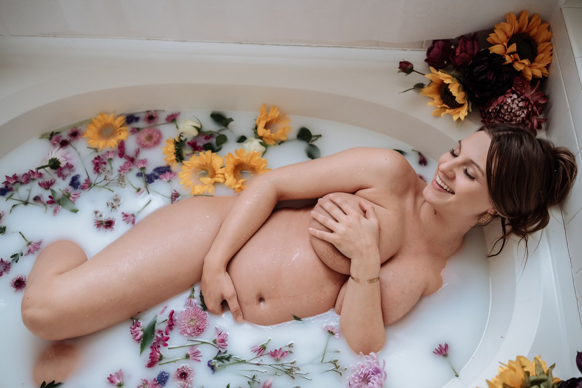 A pregnant woman is laying in a bathtub filled with milk and flowers.