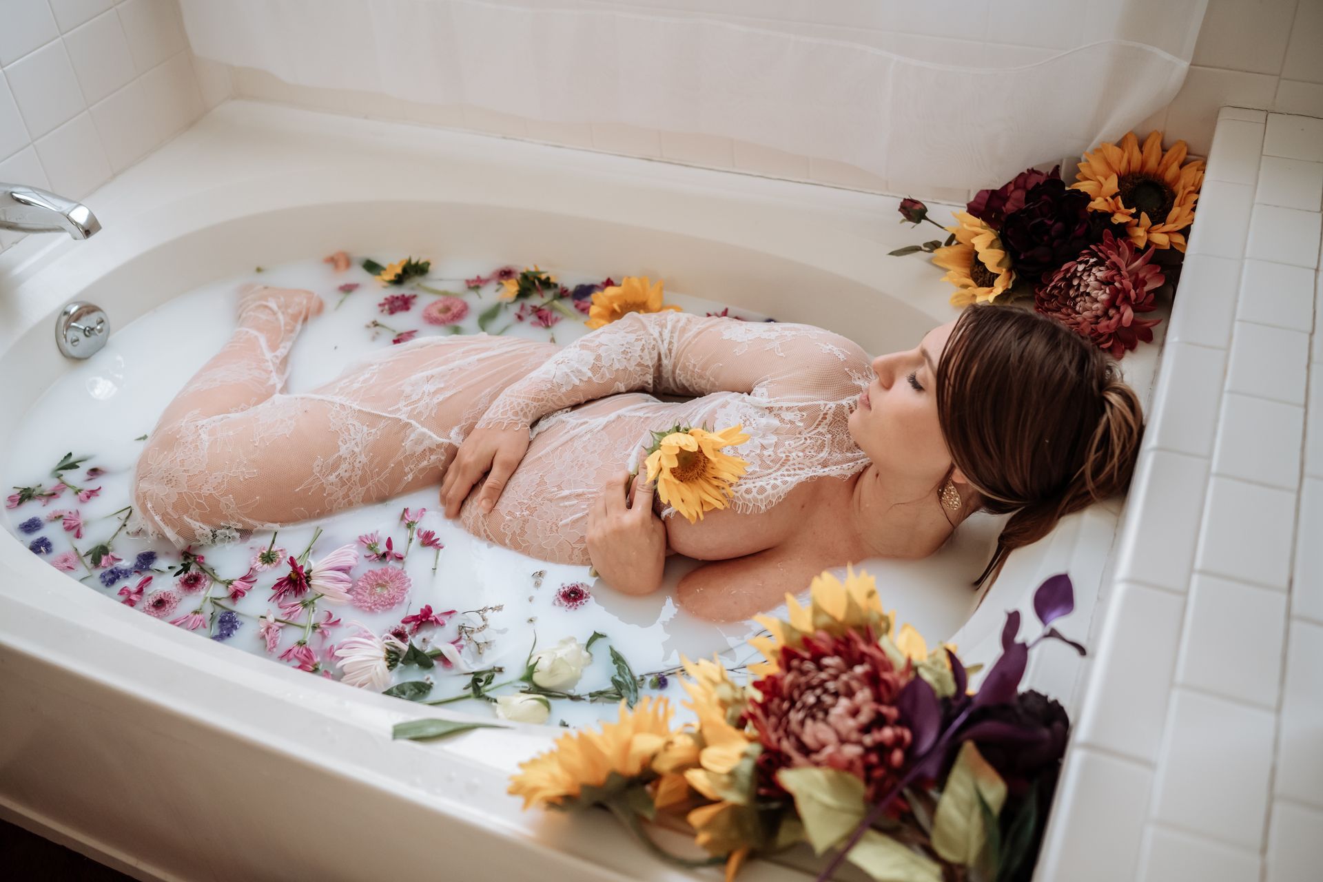 A pregnant woman is laying in a bathtub filled with milk and flowers.
