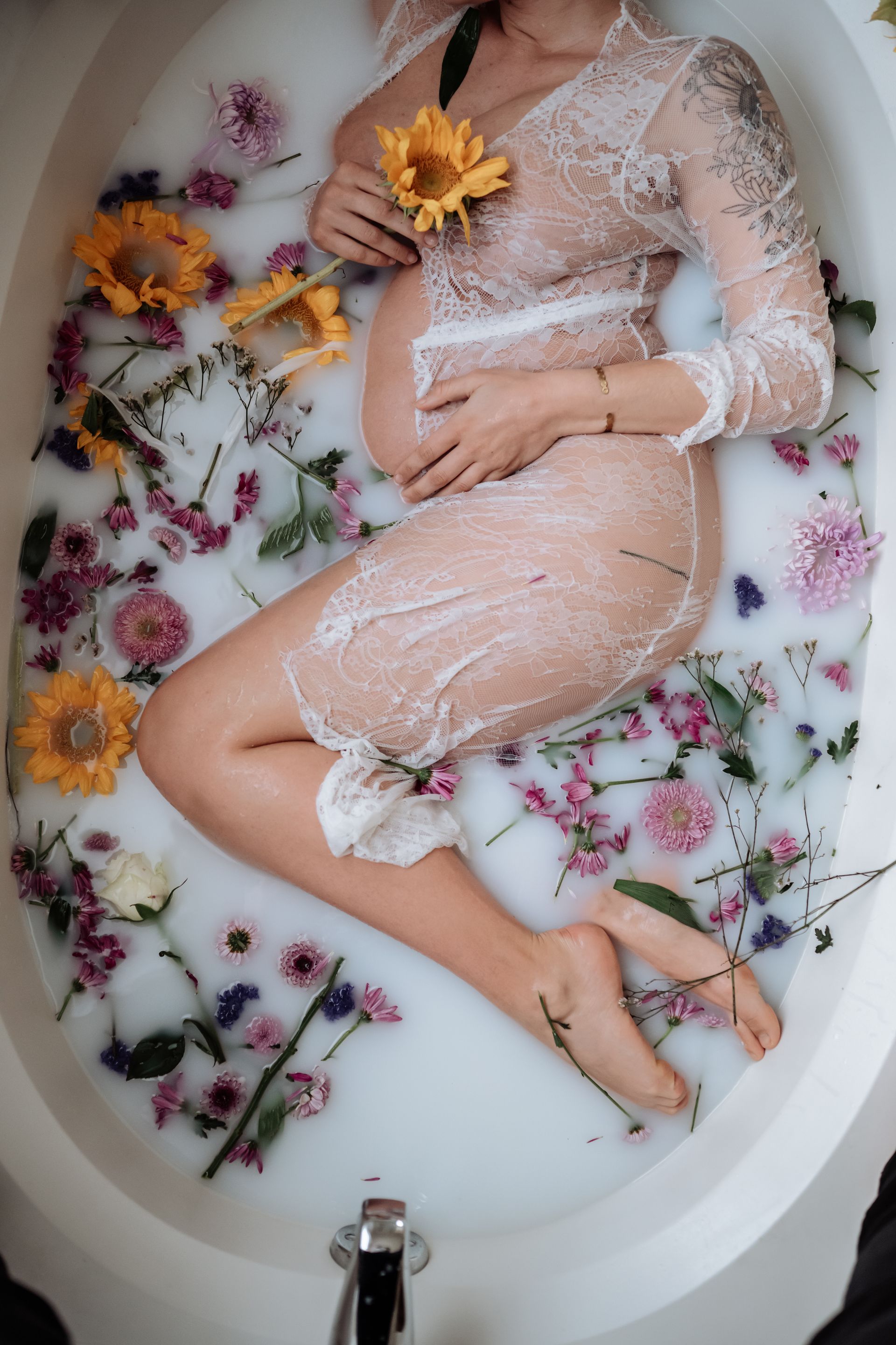 A pregnant woman is laying in a bathtub filled with milk and flowers.