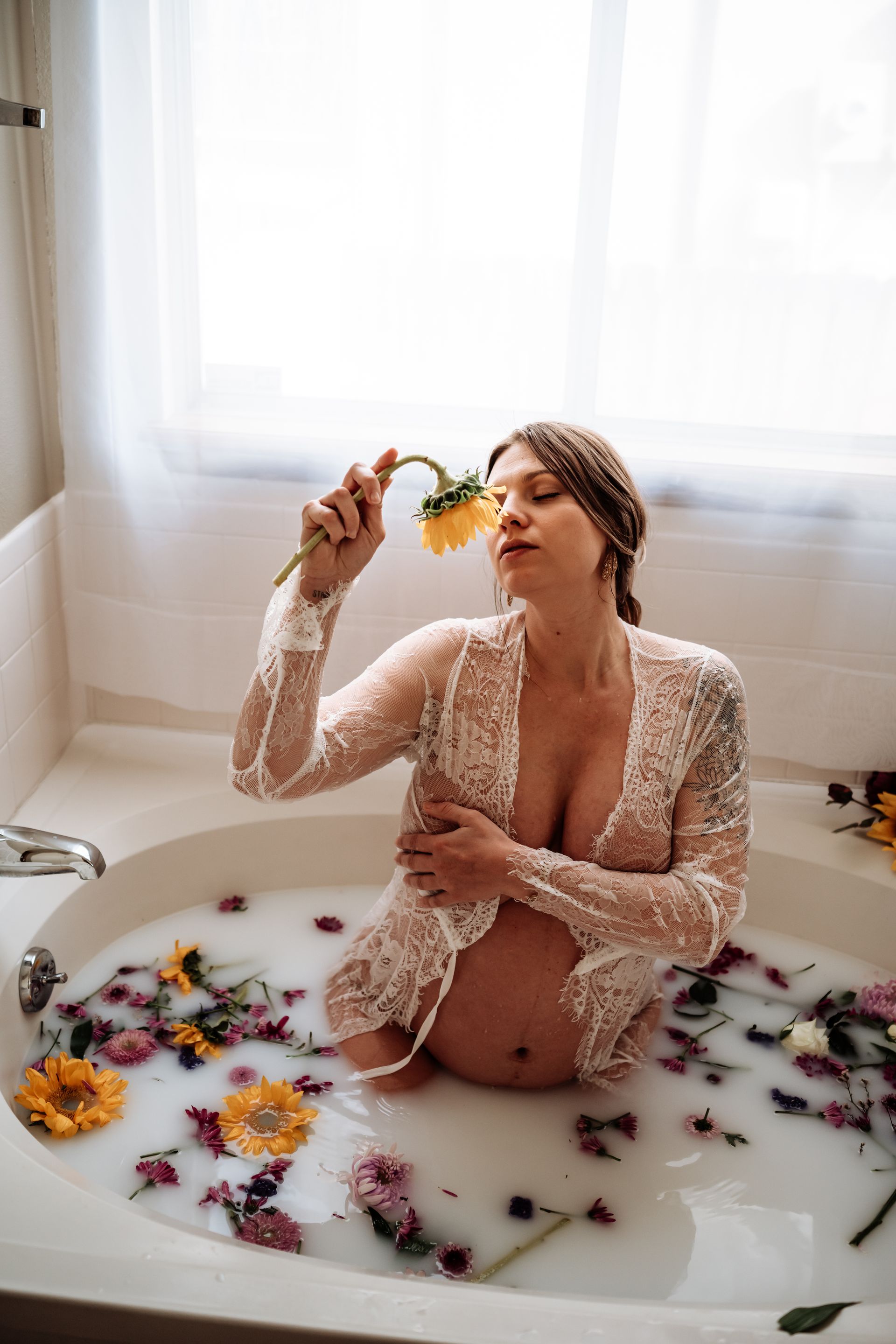 A pregnant woman is sitting in a bathtub filled with milk and flowers.