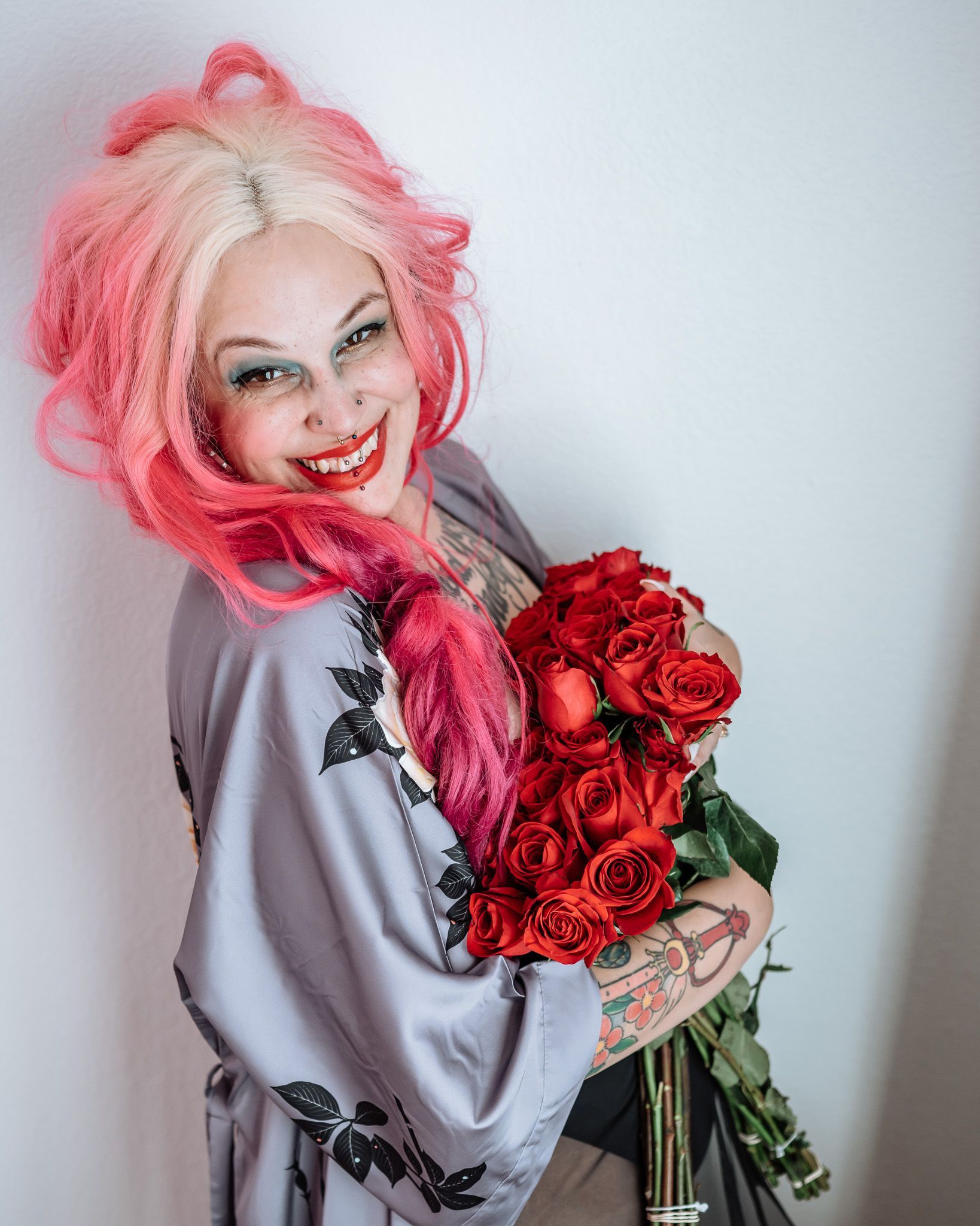 A woman with pink hair is holding a bouquet of red roses.
