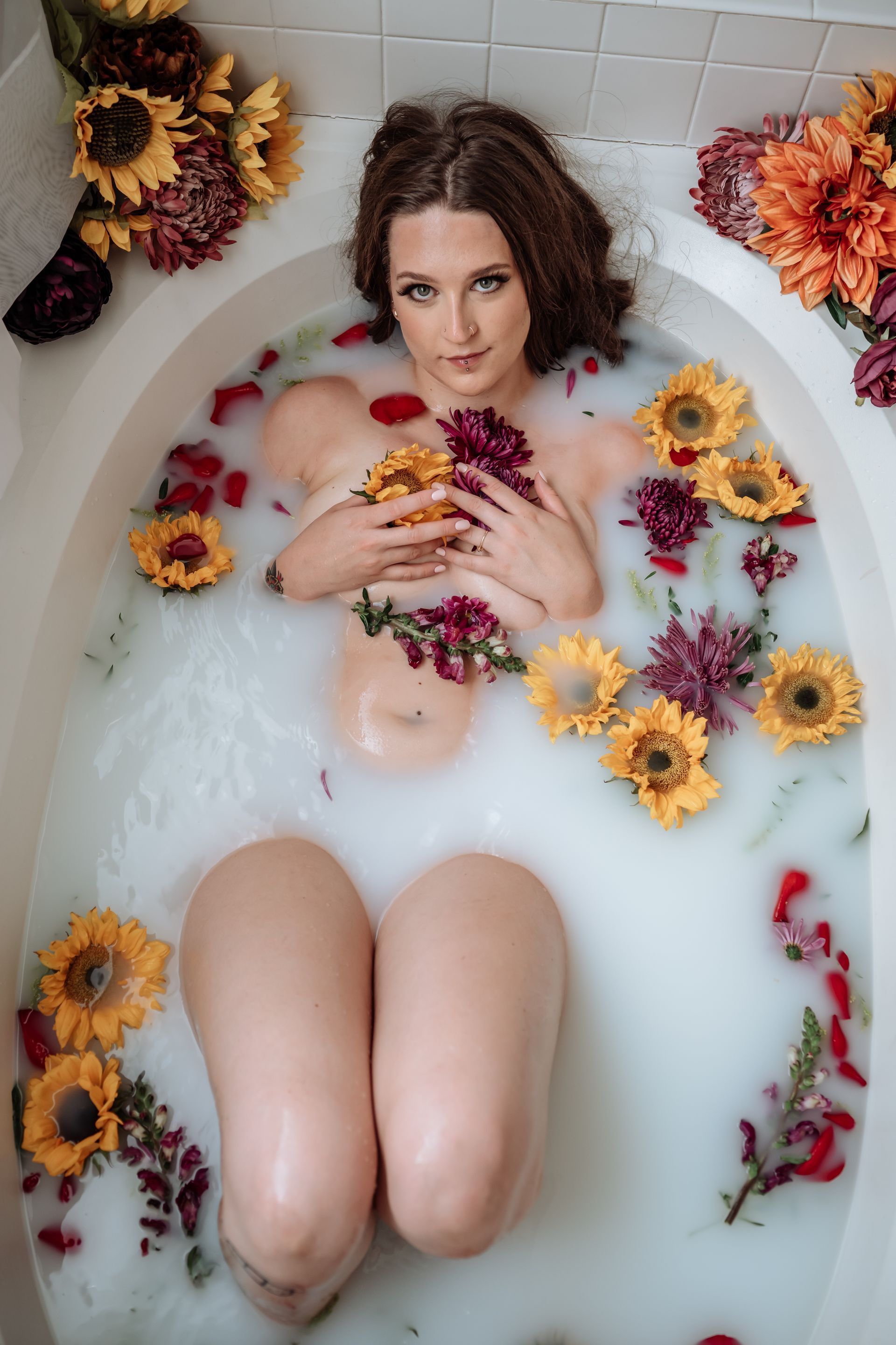 A woman is laying in a bathtub filled with milk and flowers.