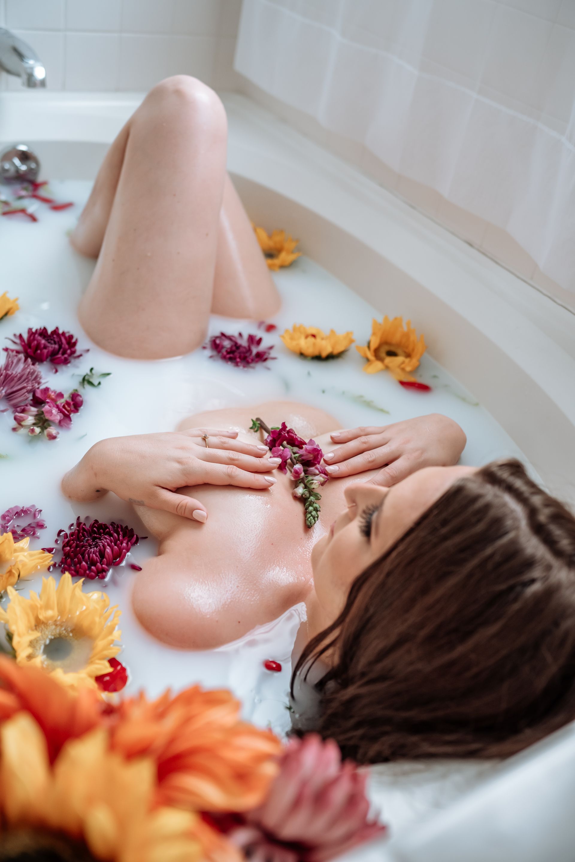 A woman is laying in a bathtub filled with milk and flowers.