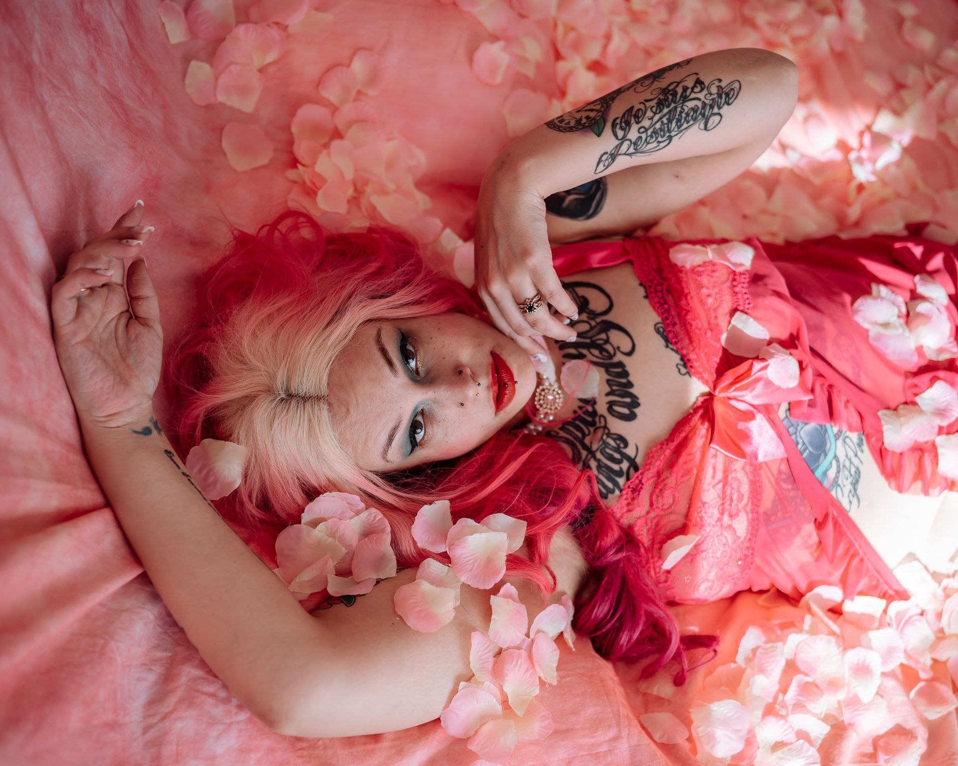a woman laying on a pink background, surrounded in flowers. 