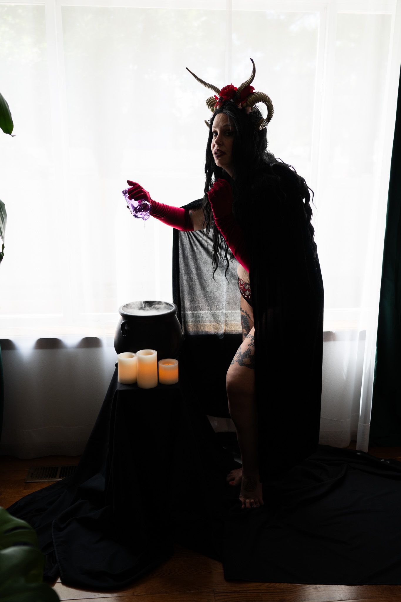 A woman in a witch costume is standing in front of a window.