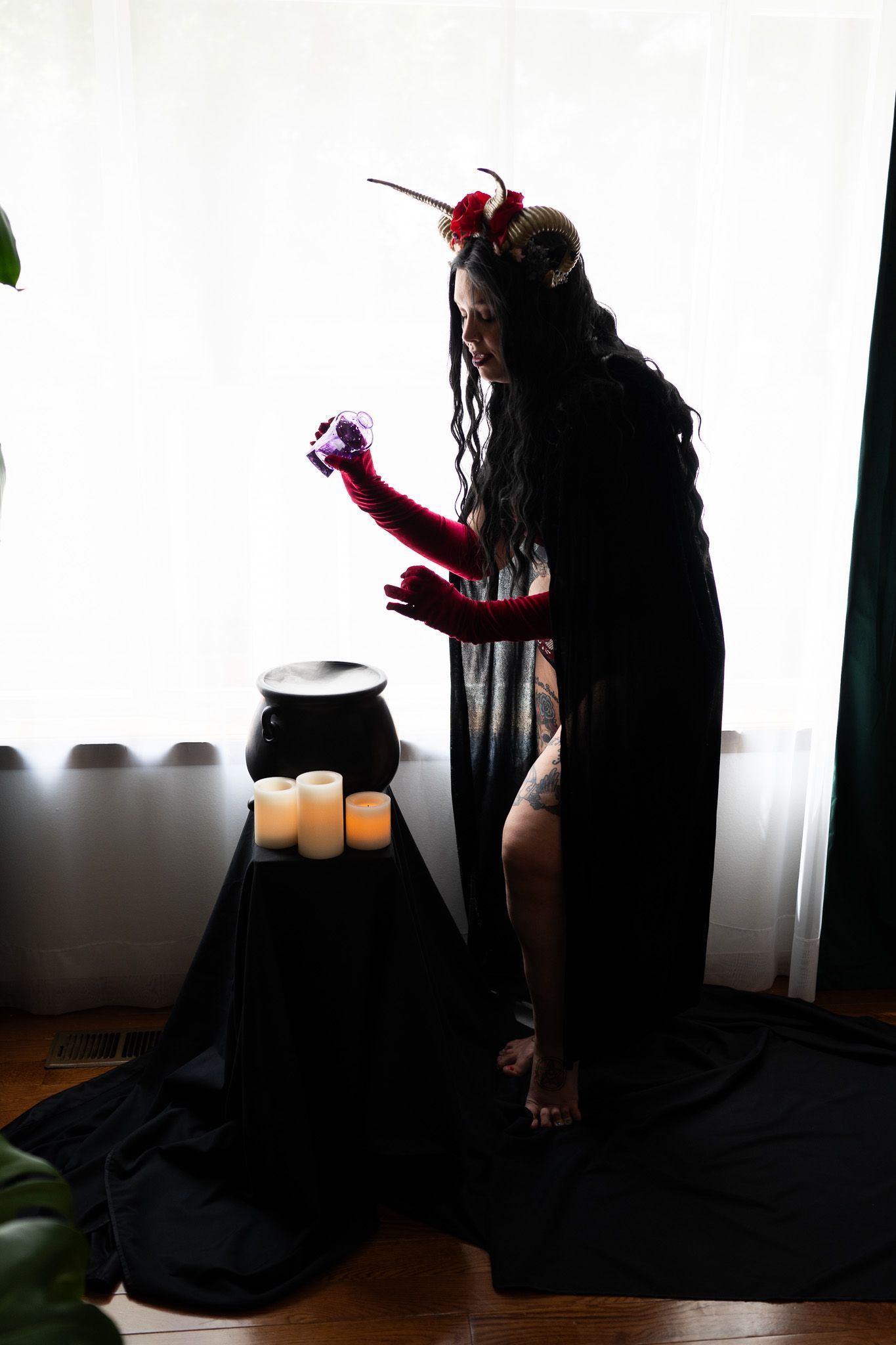 A woman in a black dress and red gloves is standing in front of a window.
