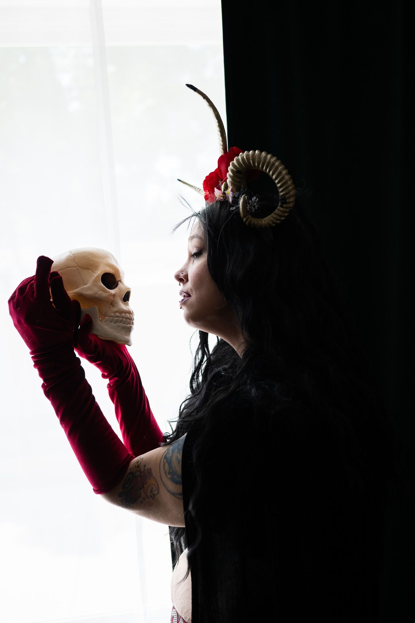 A woman in a devil costume is holding a skull in her hand.