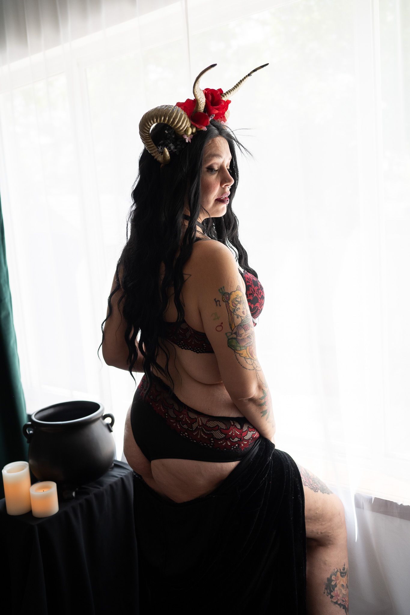 A woman in lingerie and horns is sitting on a window sill.