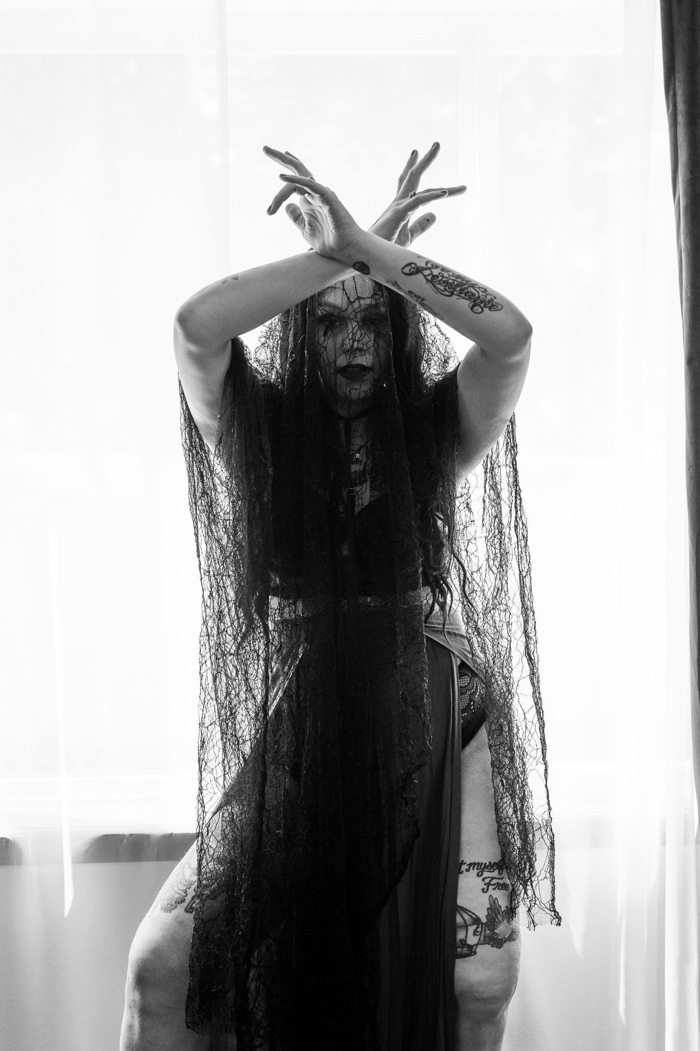 A black and white photo of a woman in a black dress standing in front of a window.