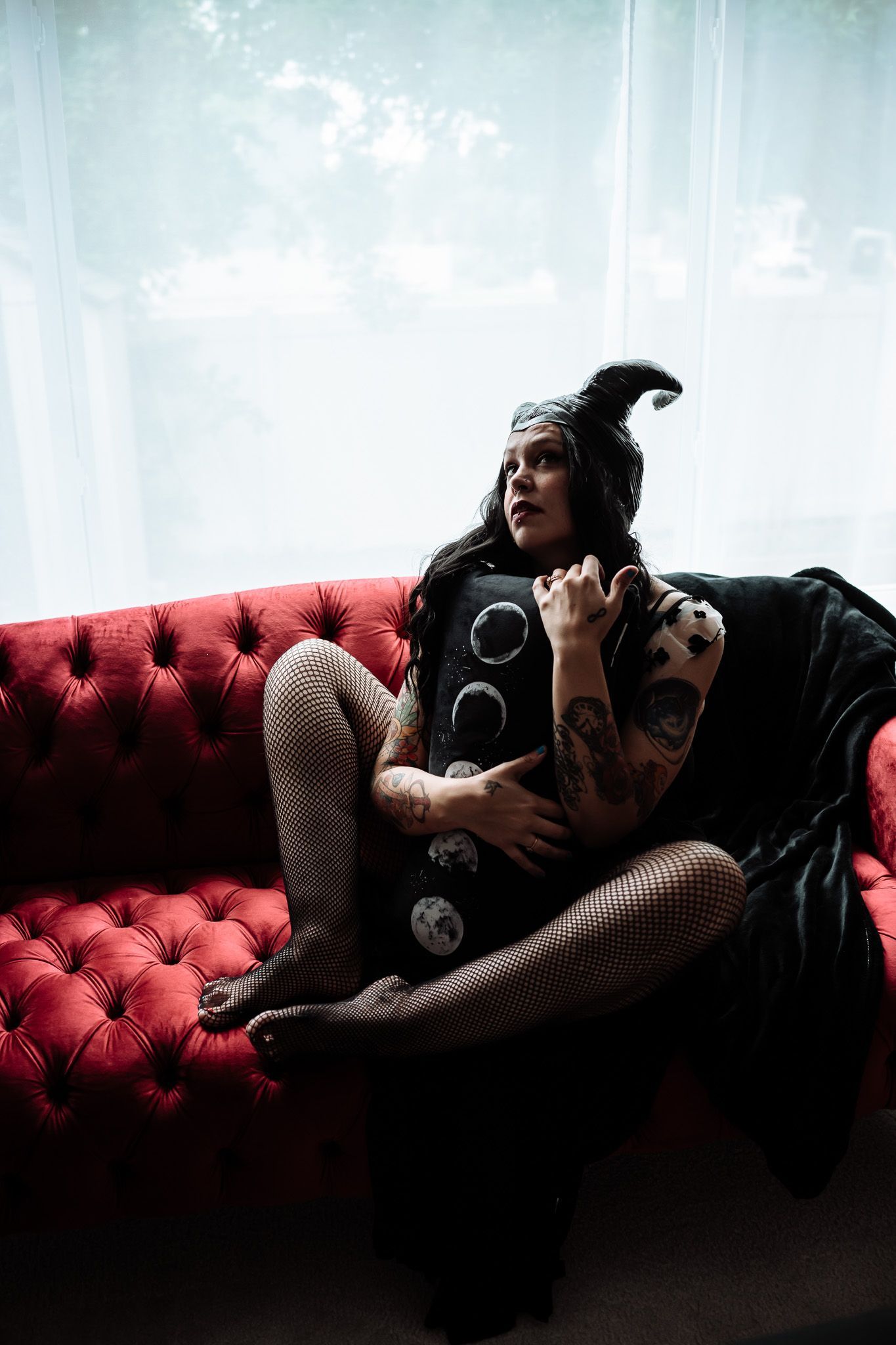A woman is sitting on a red couch holding a black pillow.