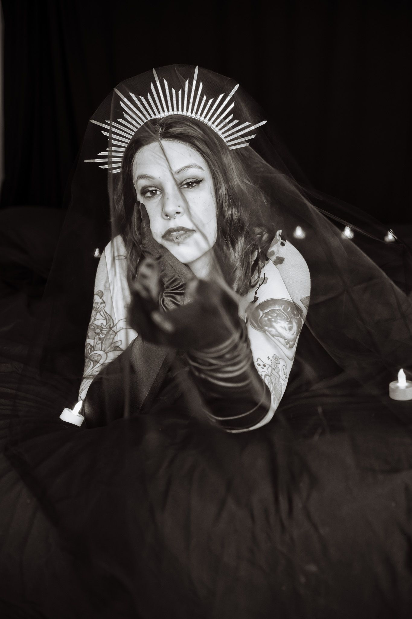 A woman in a veil and gloves is laying on a bed with candles.