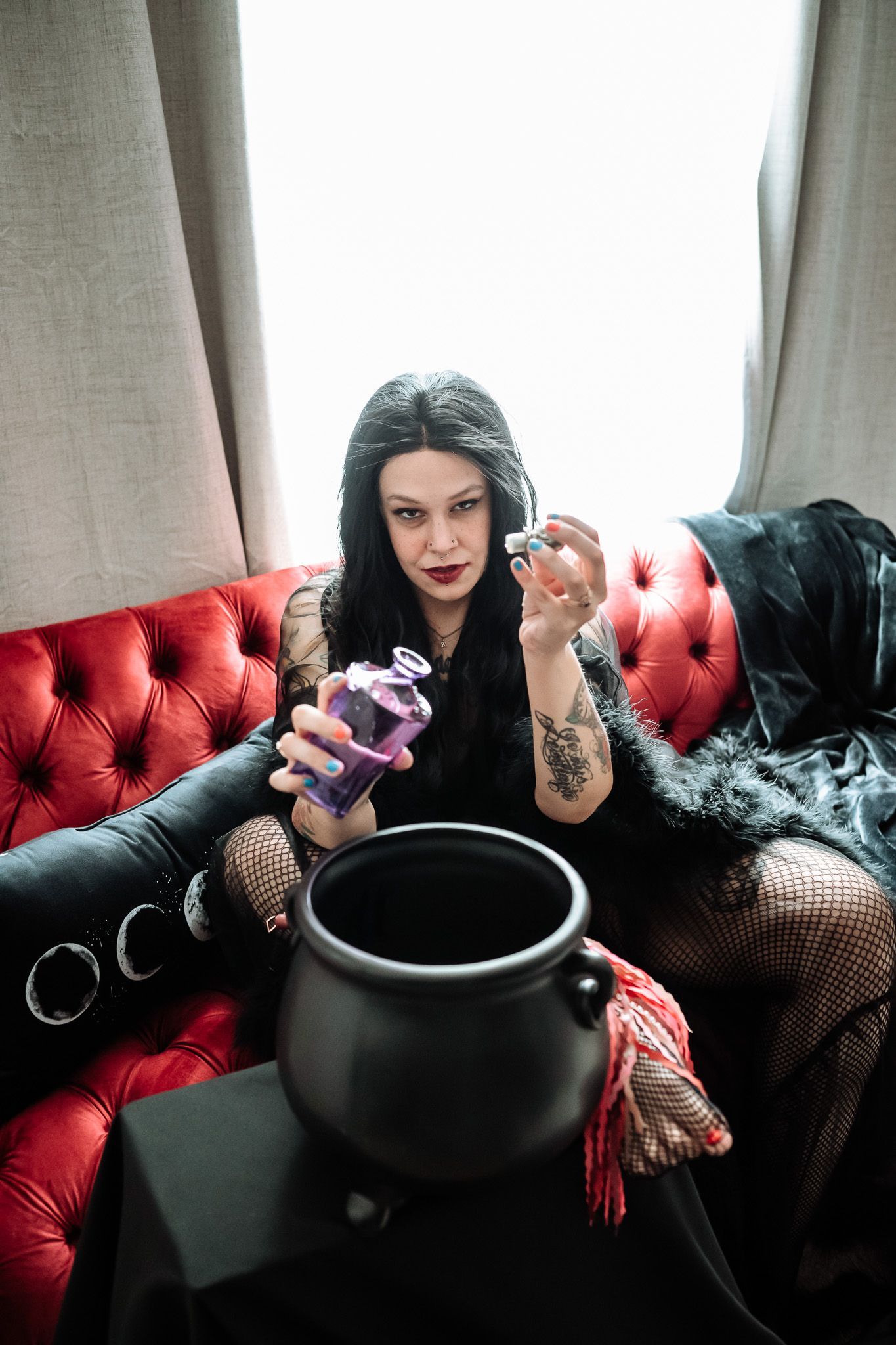 A woman is sitting on a red couch holding a cauldron and a bottle.
