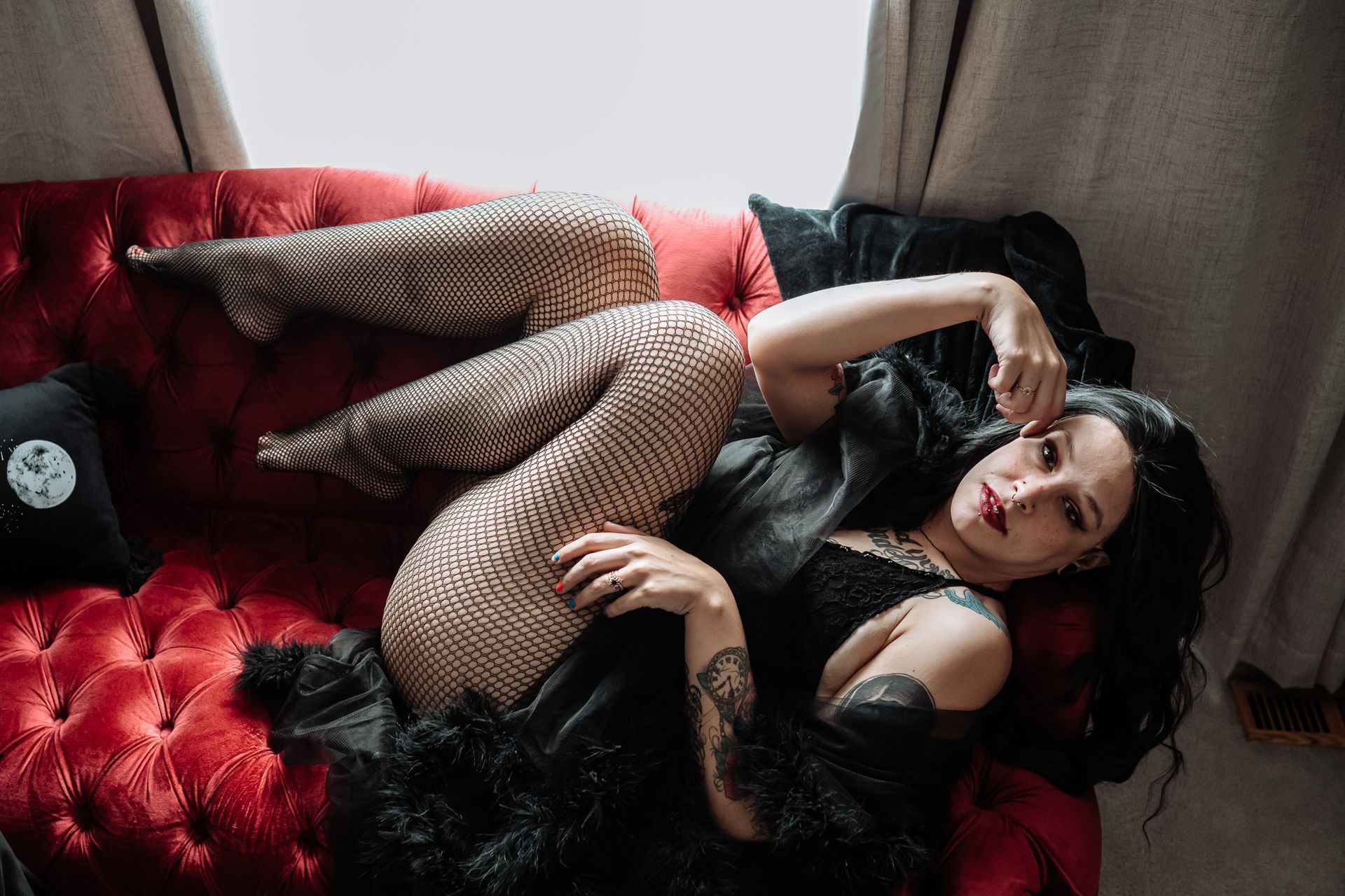 A woman is laying on a red couch with her legs crossed.