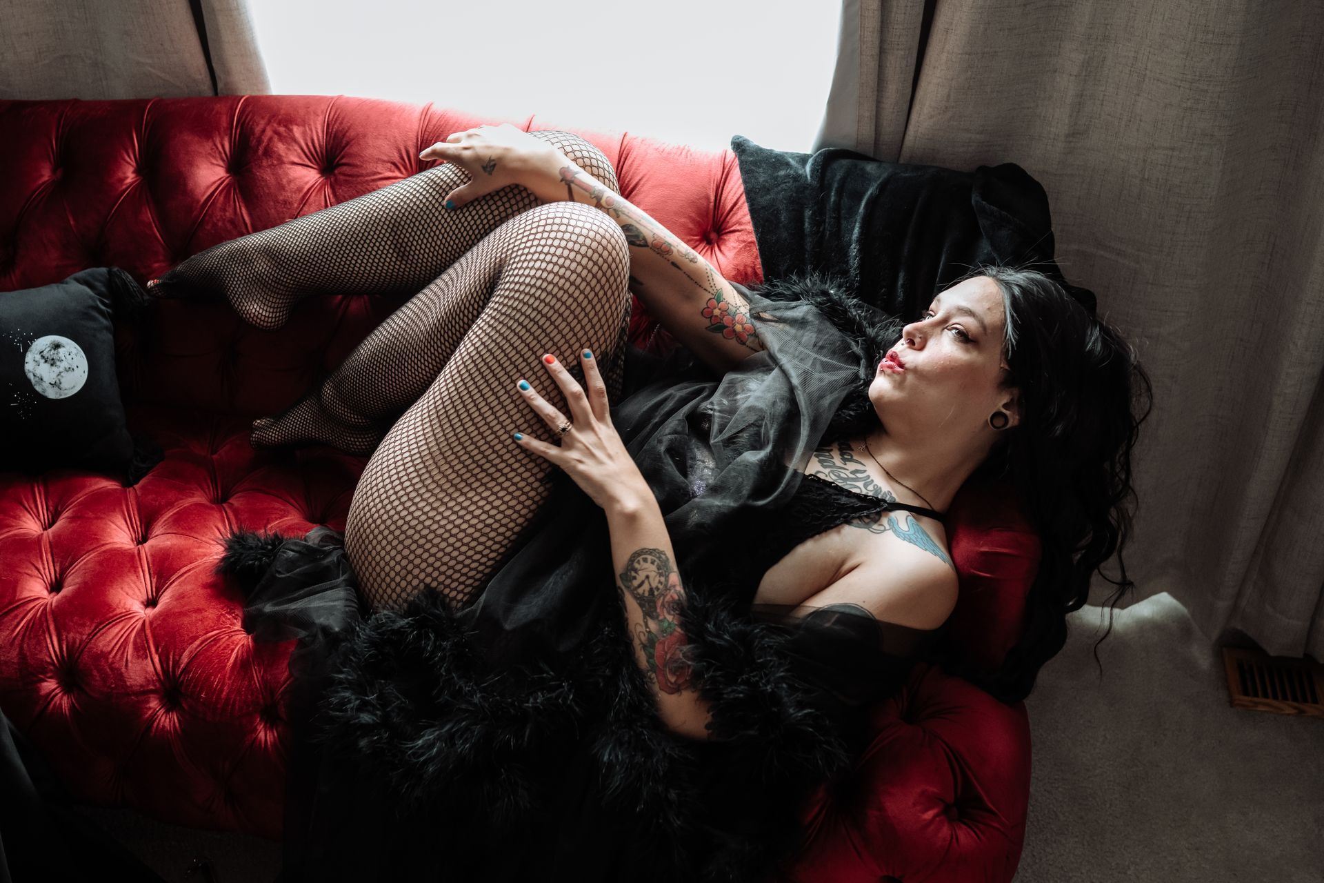 A woman in a black dress and fishnet stockings is laying on a red couch.