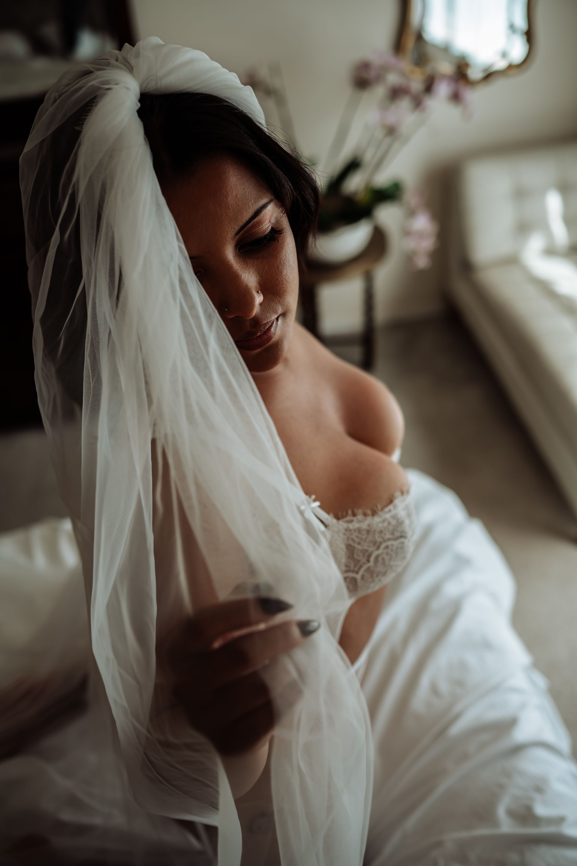 A woman in a wedding dress and veil is sitting on a bed.