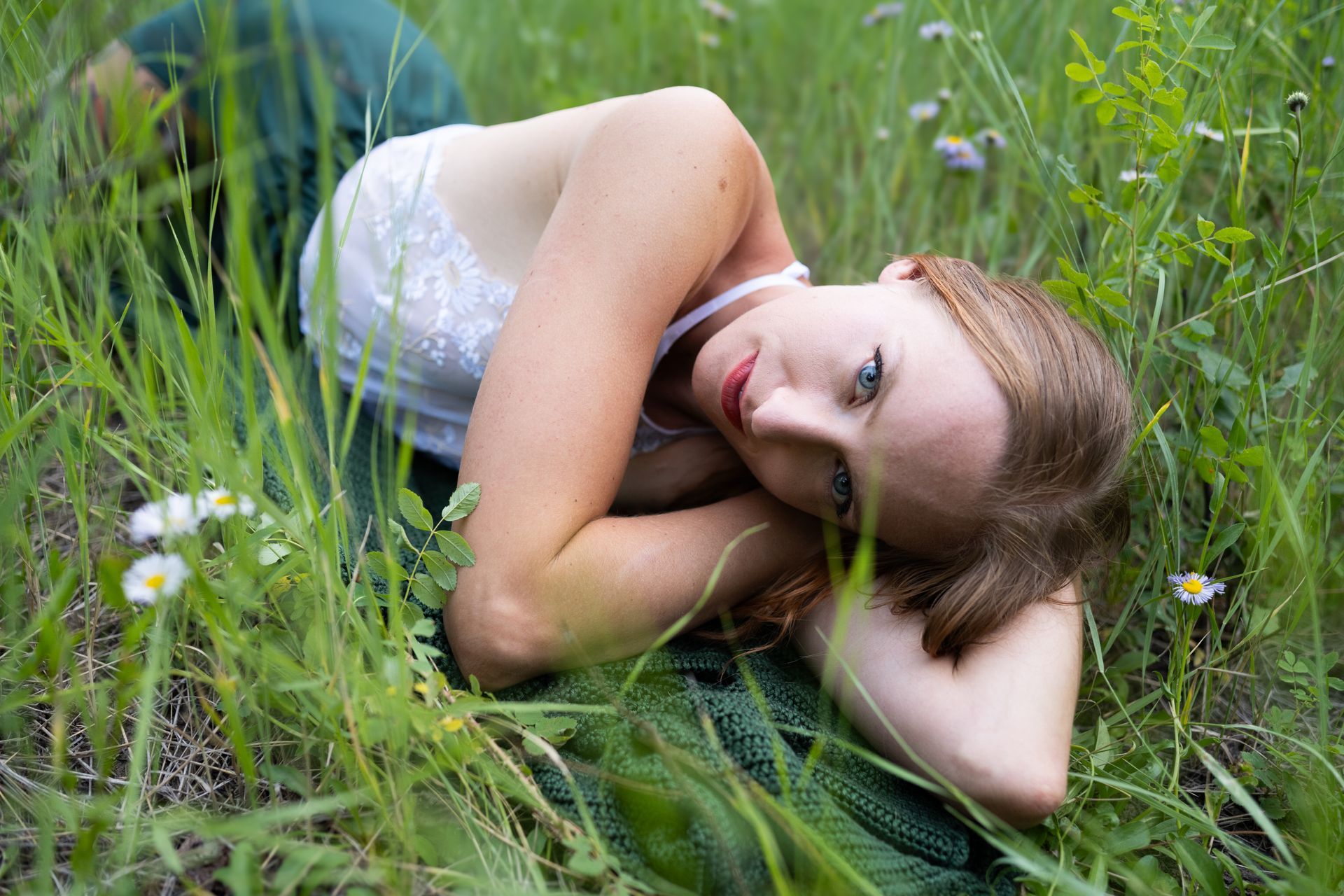 A woman is laying in the grass with her head on her arms.