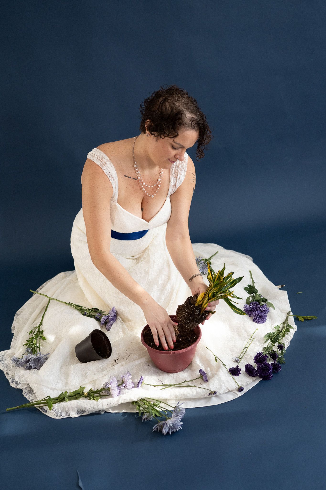 A woman in a white dress is kneeling down and putting a plant in a pot.