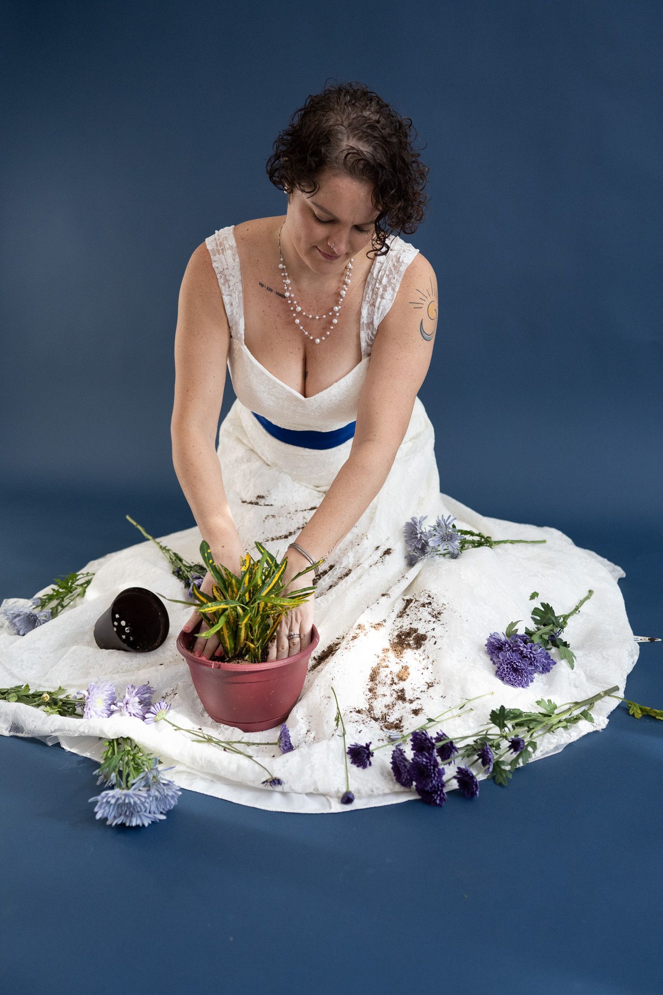 A woman in a white dress is kneeling down with flowers around her