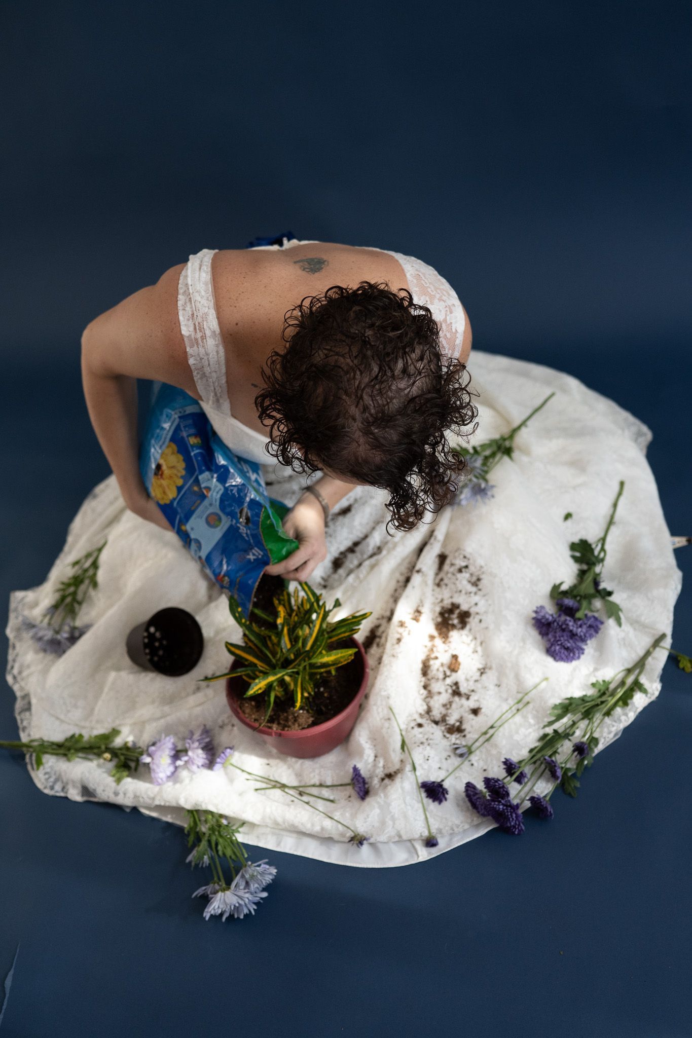 A woman in a white dress is watering a potted plant.