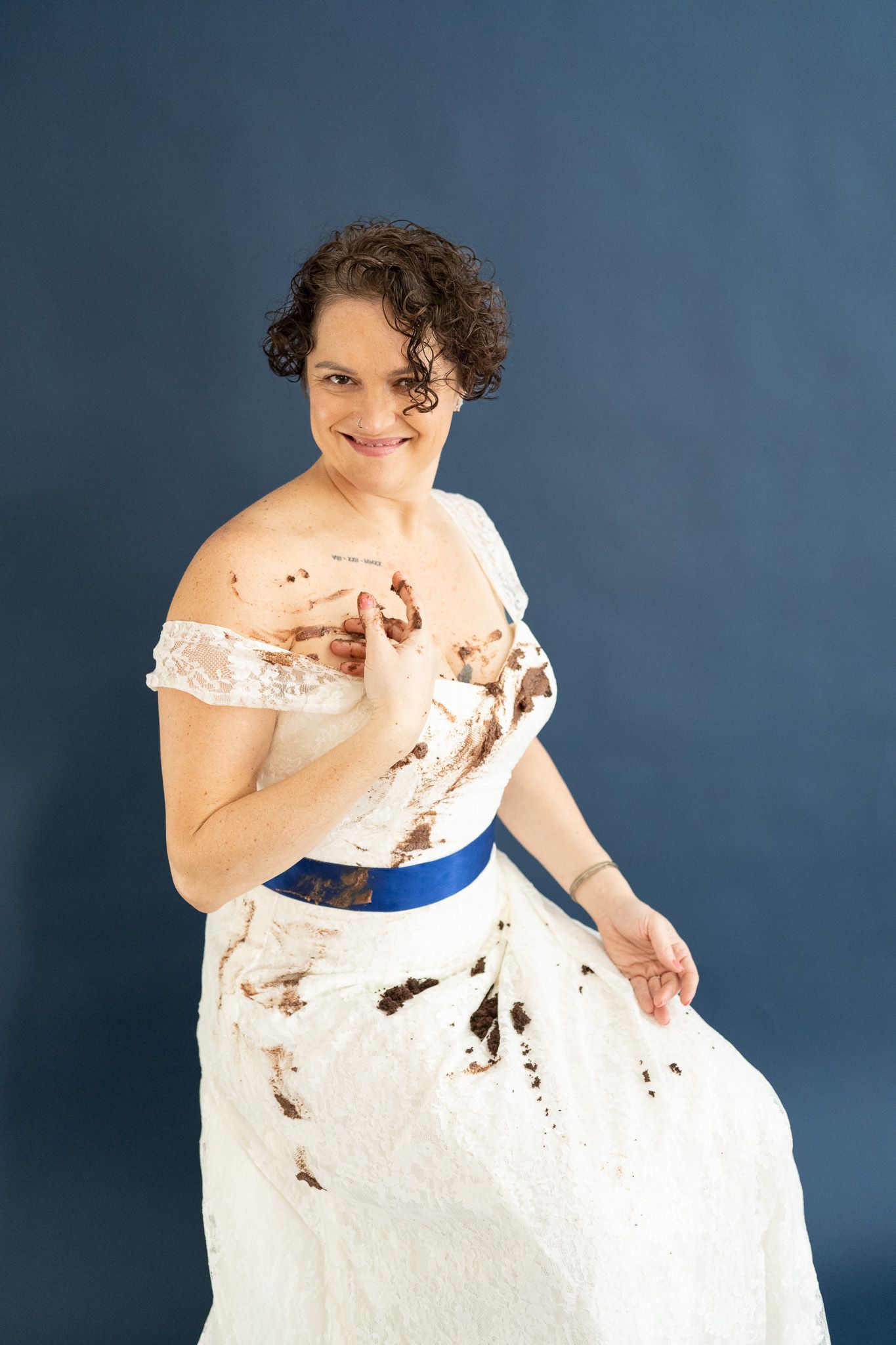 A woman in a white dress is sitting in front of a blue wall.