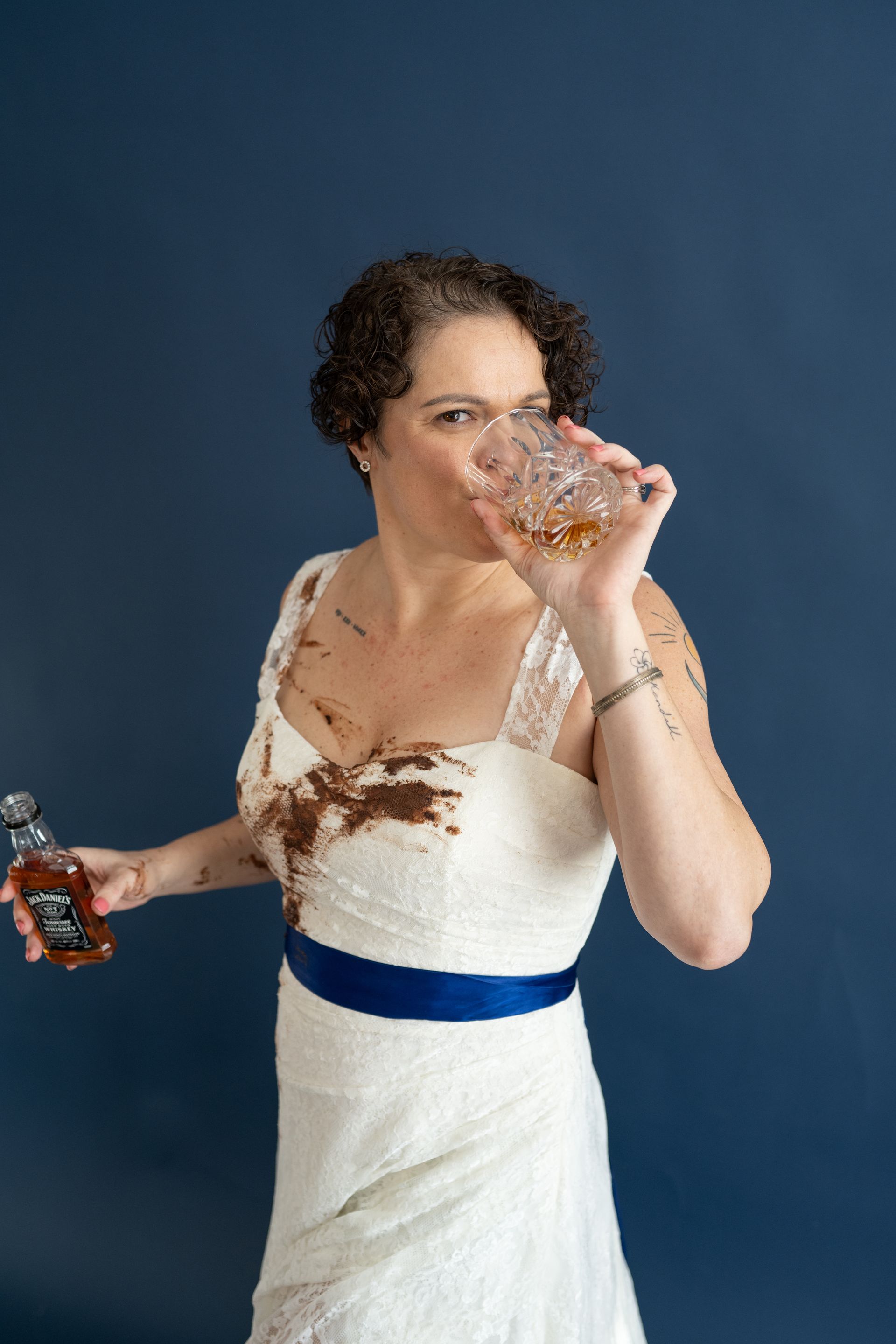 A woman in a wedding dress is drinking from a glass while holding a bottle of whiskey.