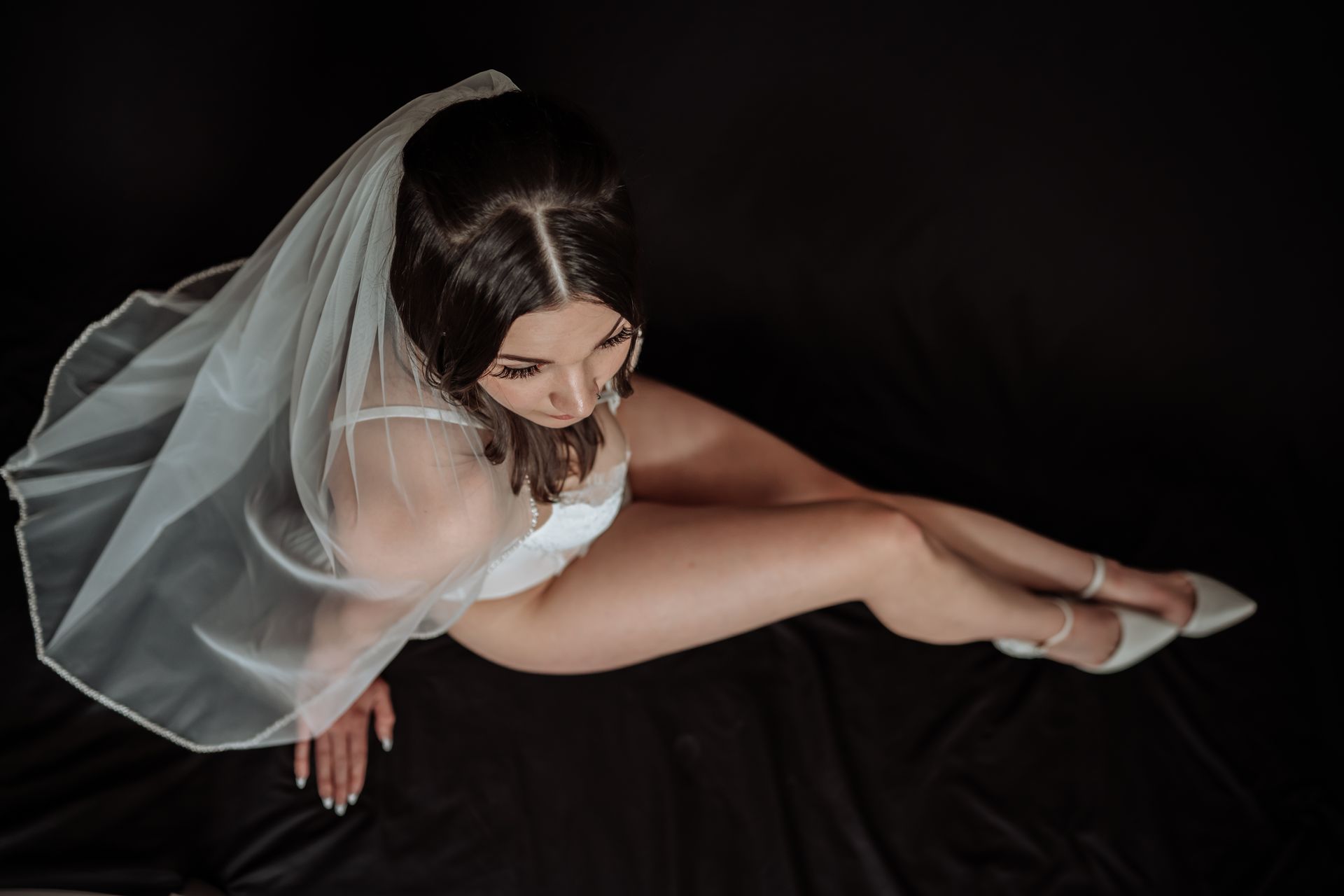 A woman in white lingerie with a black background, wearing a veil. 