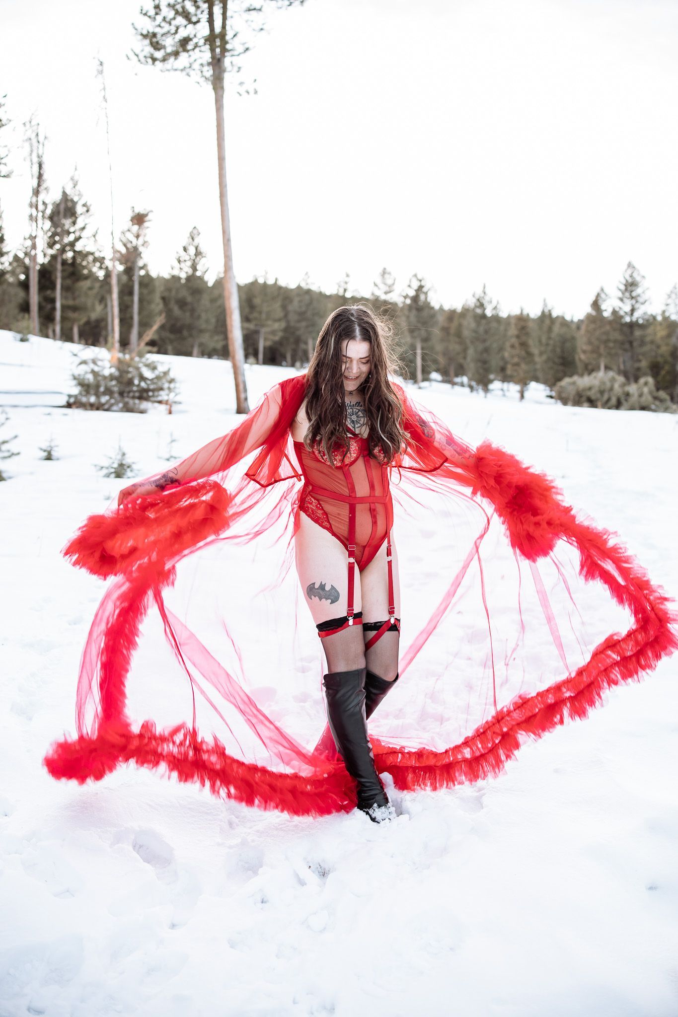 A woman in lingerie and a red cape is standing in the snow.
