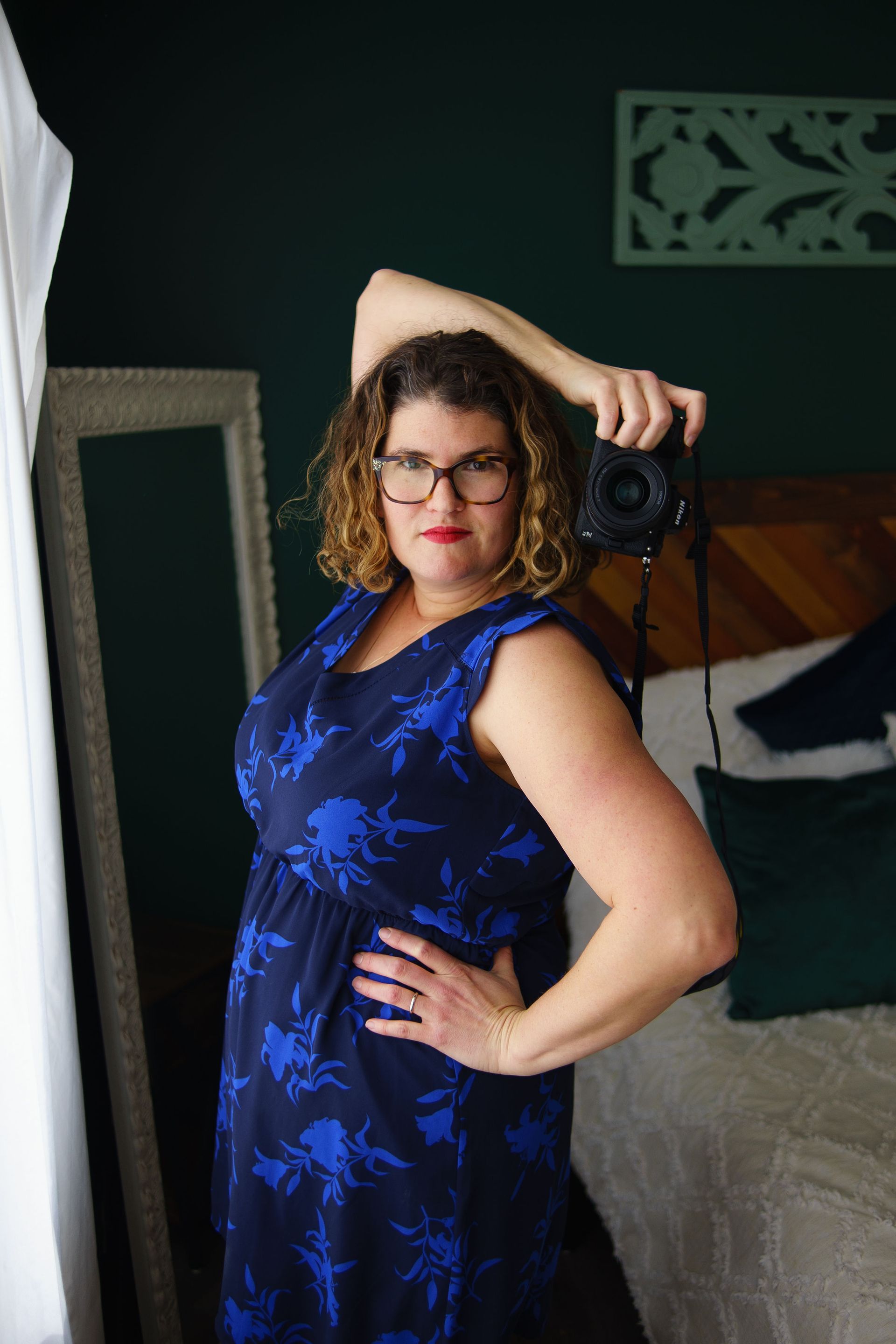 A woman in a blue dress is taking a picture of herself with a camera.