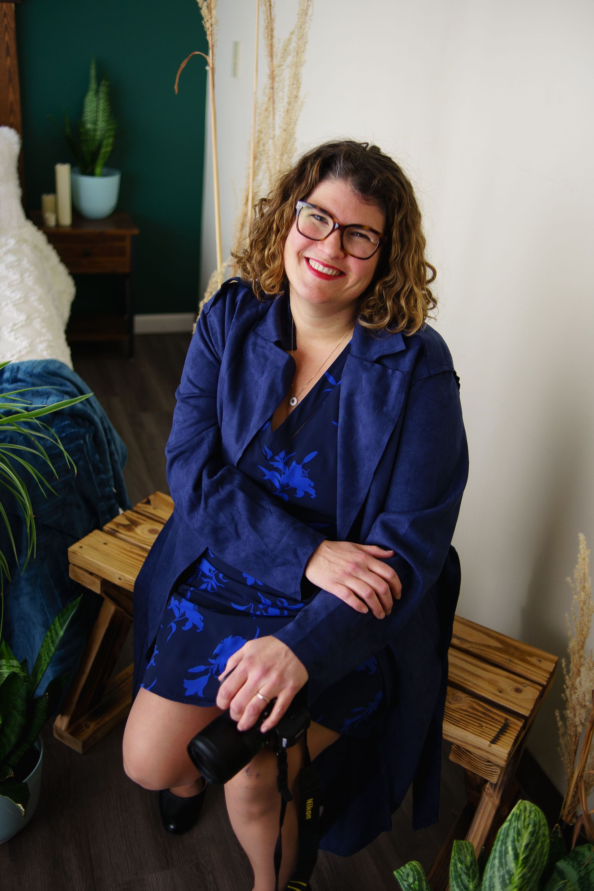A woman in a blue dress is sitting on a wooden bench holding a camera.