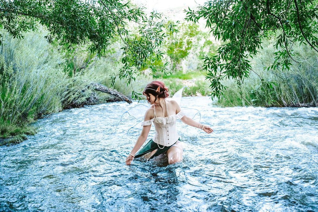 A woman is kneeling in a river surrounded by trees.