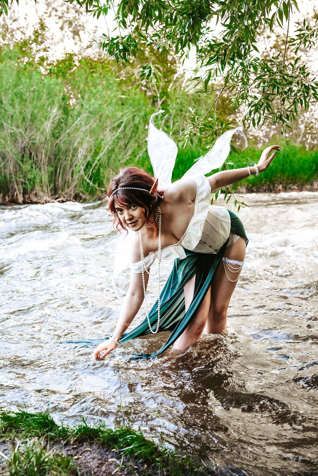 A woman dressed as a fairy is kneeling in a river.