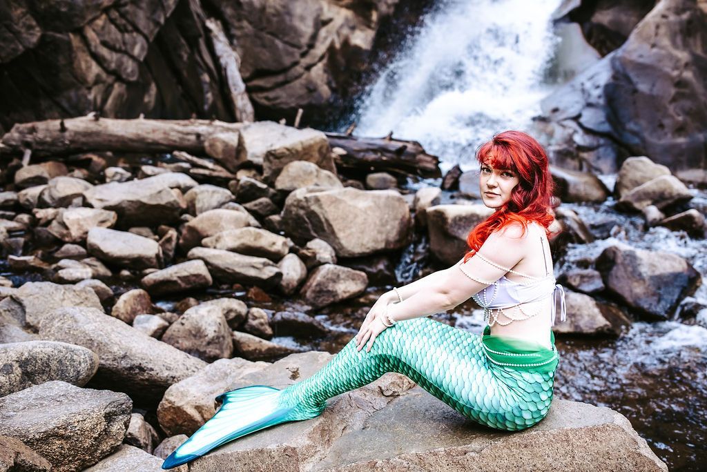 A mermaid is sitting on a rock in front of a waterfall.