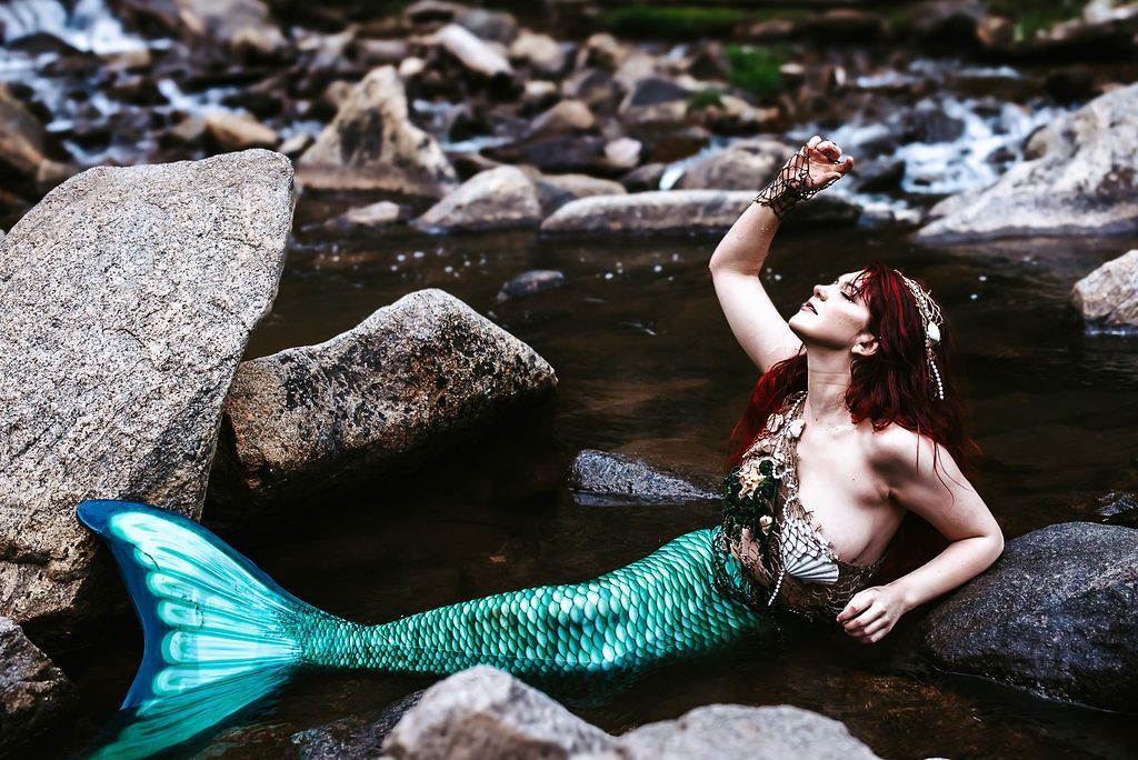 A mermaid is laying on a rock in the water.