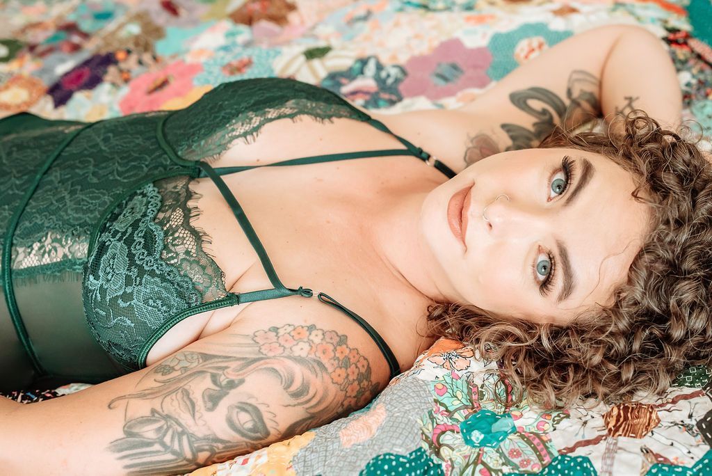 A woman in green lingerie is lying on a quilt on a bed.
