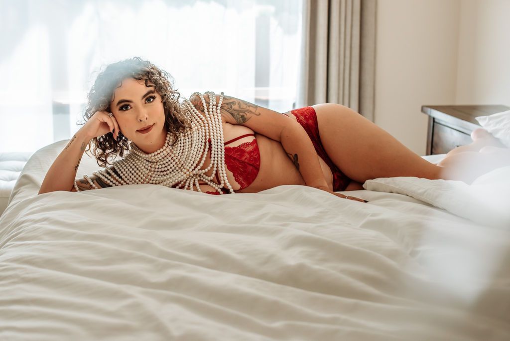 a woman laying on her side in a pearl body piece and red lingerie.