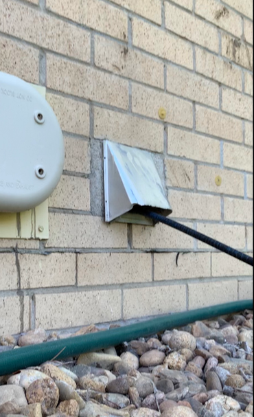 Black cable plugged into a wall-mounted metal outlet on a brick exterior wall.