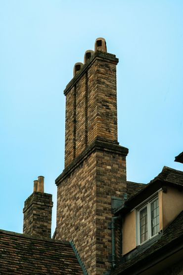 Brick chimneys rising above a tiled roof against a pale blue sky.