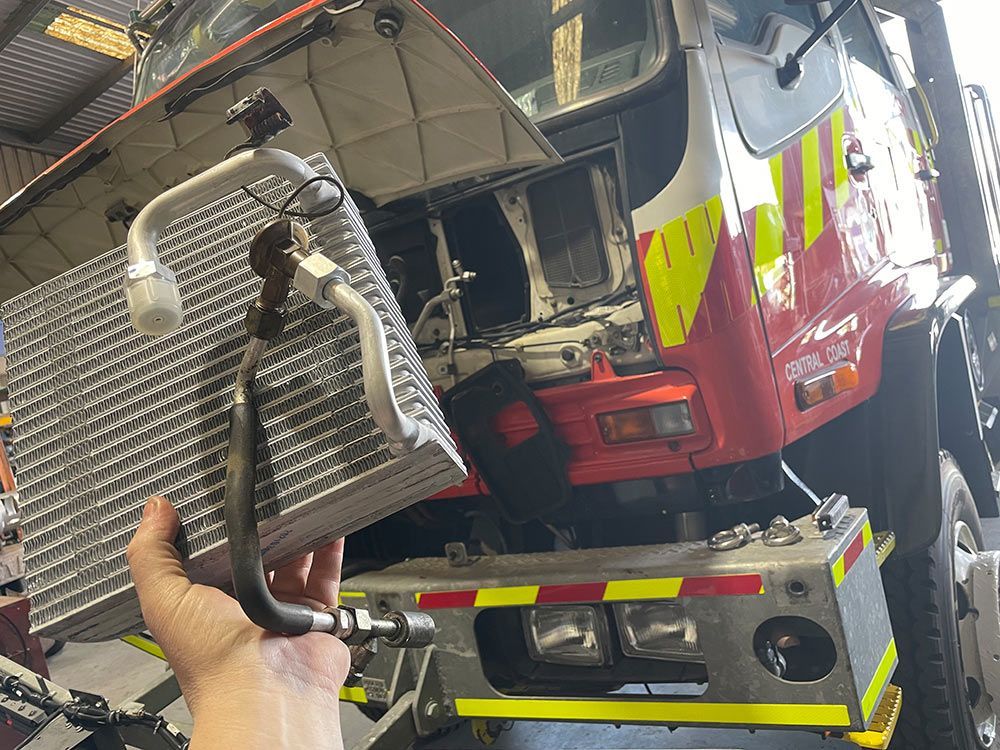 A Person Is Holding A Radiator In Front Of A Fire Truck — Autocool Air Conditioning in Raymond Terrace, NSW