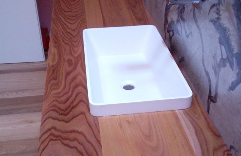 Lavabo rettangolare bianco su un piano di lavoro in legno accanto a un divano a fantasia.